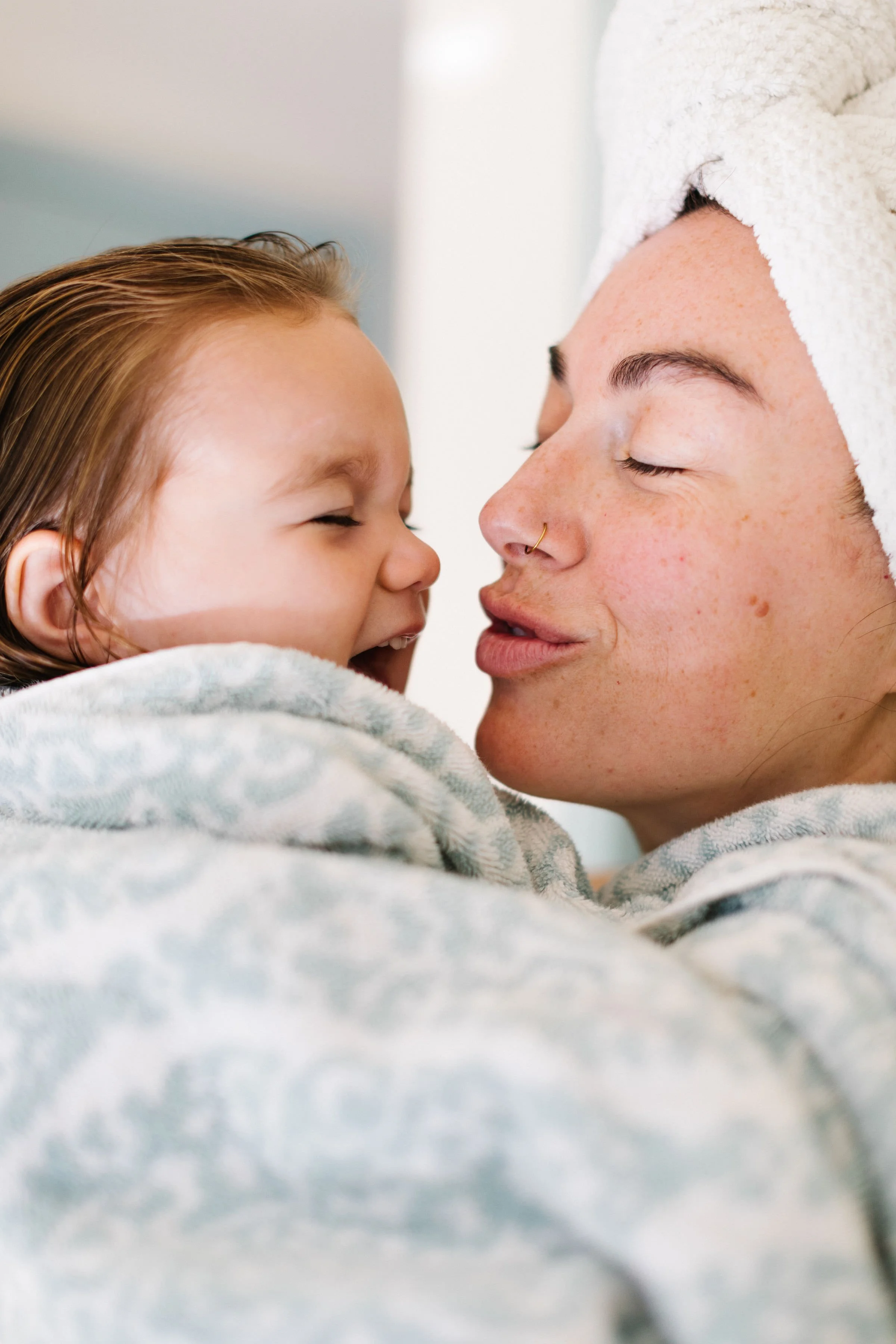 A mom with her hair wrapped in a towel holds her daughter.