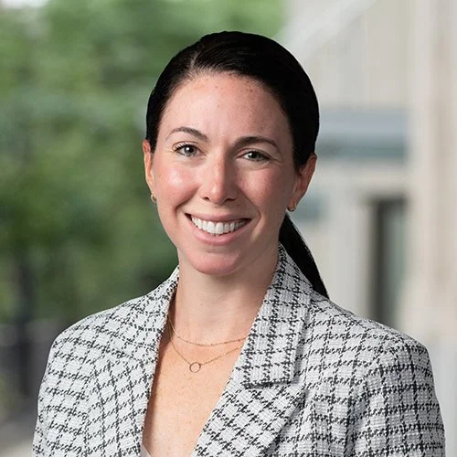 Megan Senese, a marketing and sales expert for professional service firms, smiling, wearing a checkered blazer, standing outdoors with a blurred background.