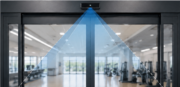 Security camera mounted on a glass door projecting a blue laser scan pattern across the entrance of a gym.