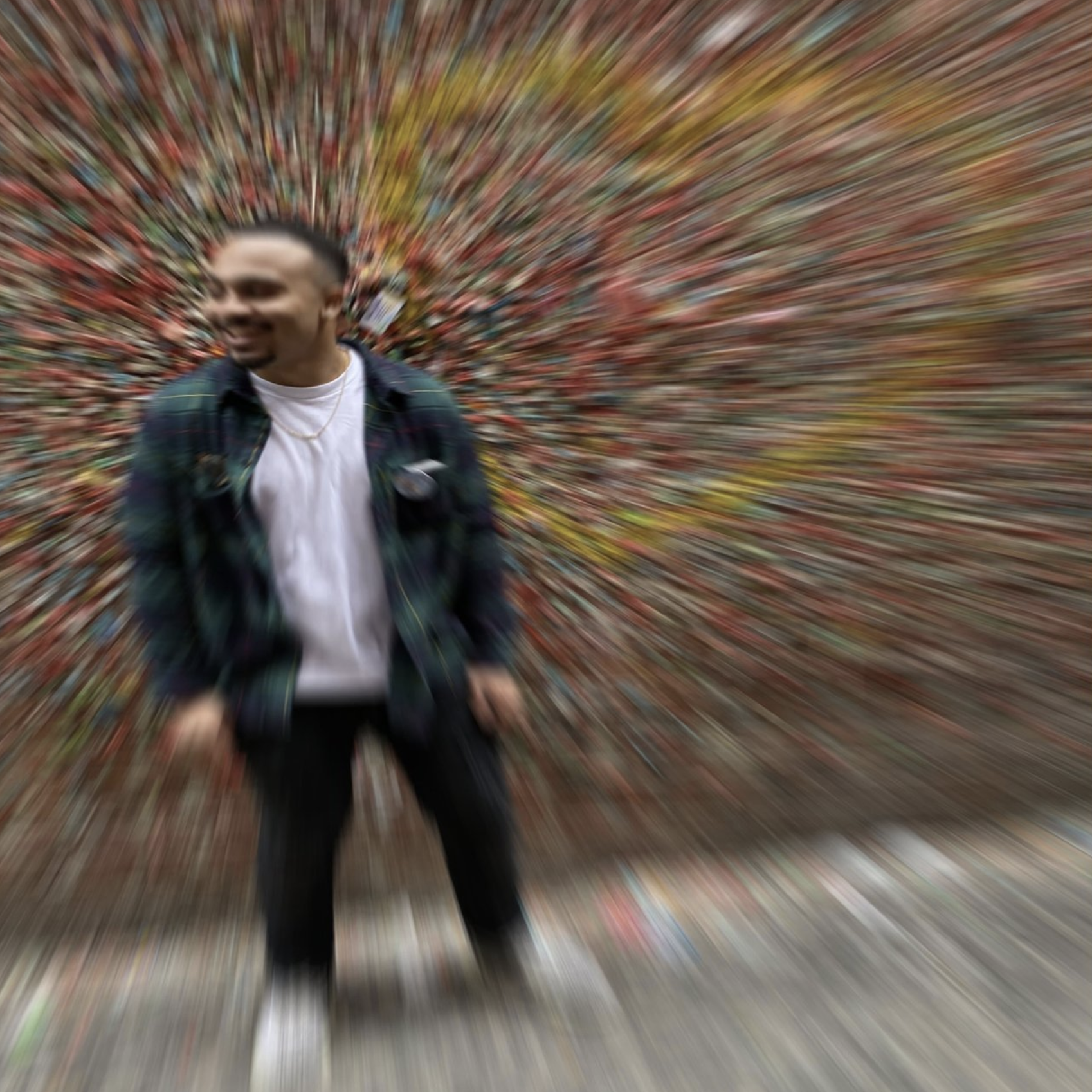 A blurry photo of a man standing outdoors in front of a colorful, autumnal background.