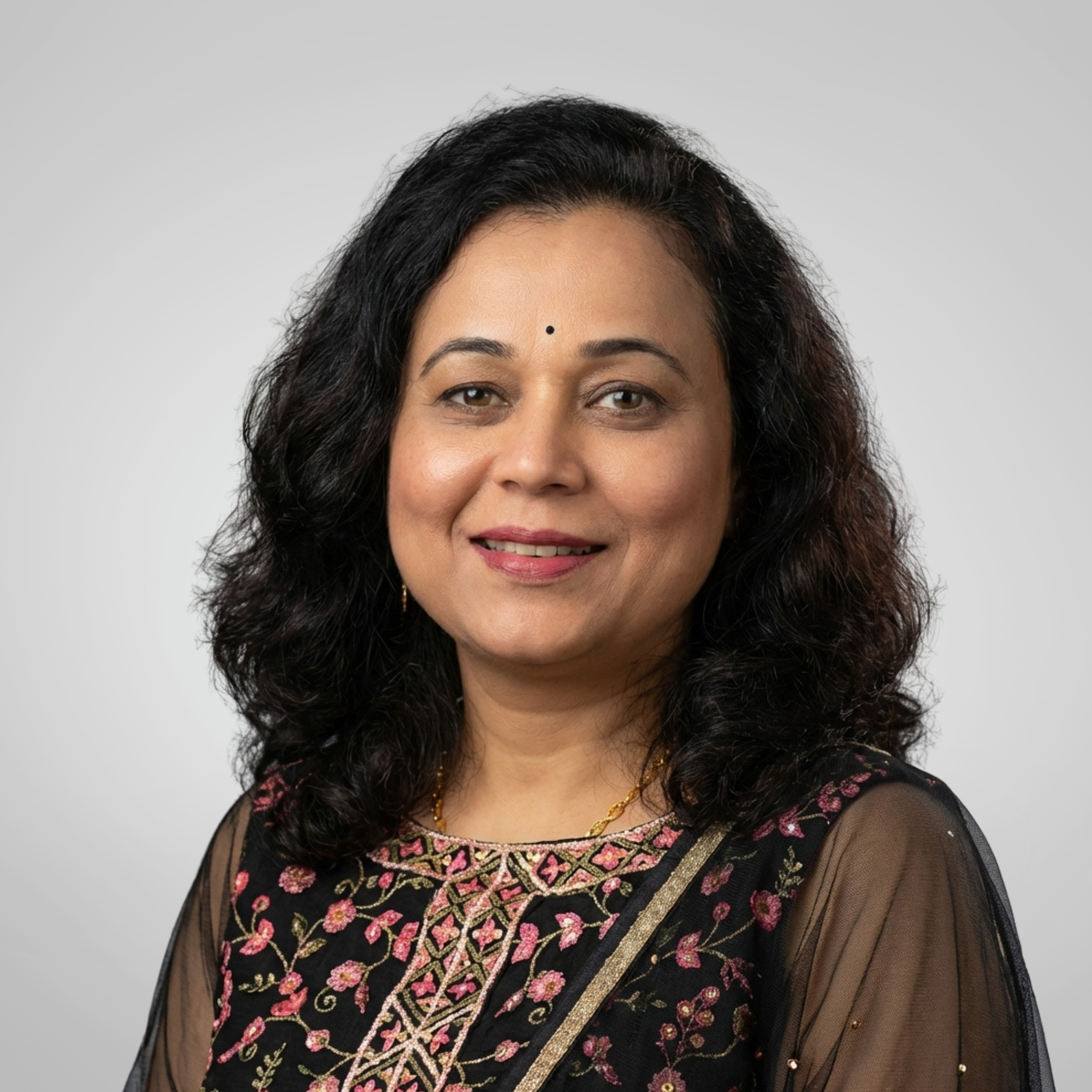 A professional headshot of a smiling woman with black hair, wearing traditional Indian attire.