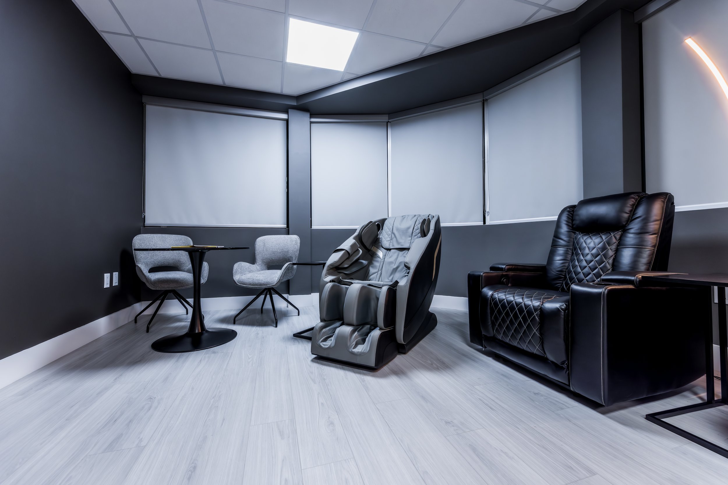 Modern lounge area with massage chair, two gray chairs, and black recliner