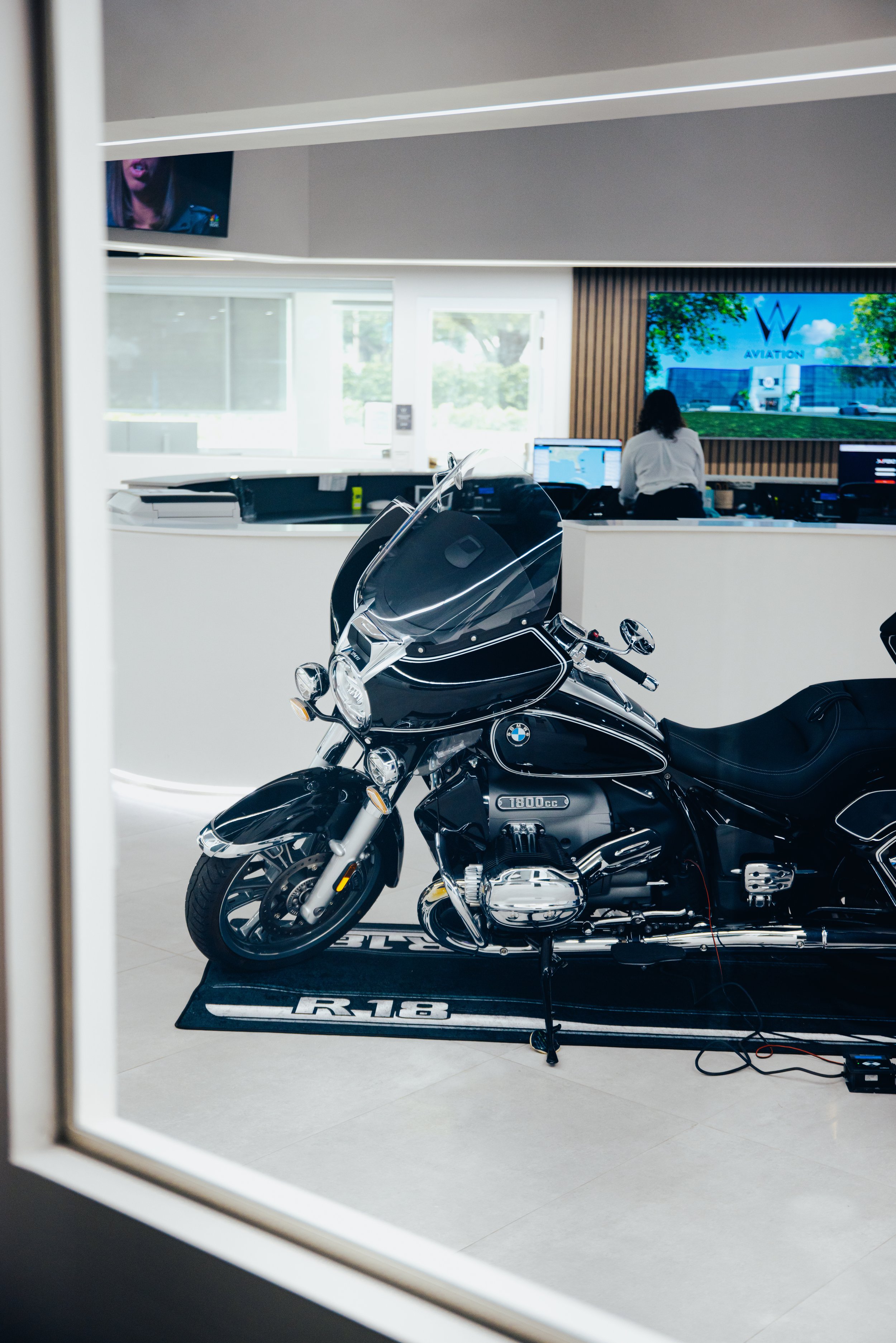 Black BMW R18 motorcycle displayed indoors near a reception desk.