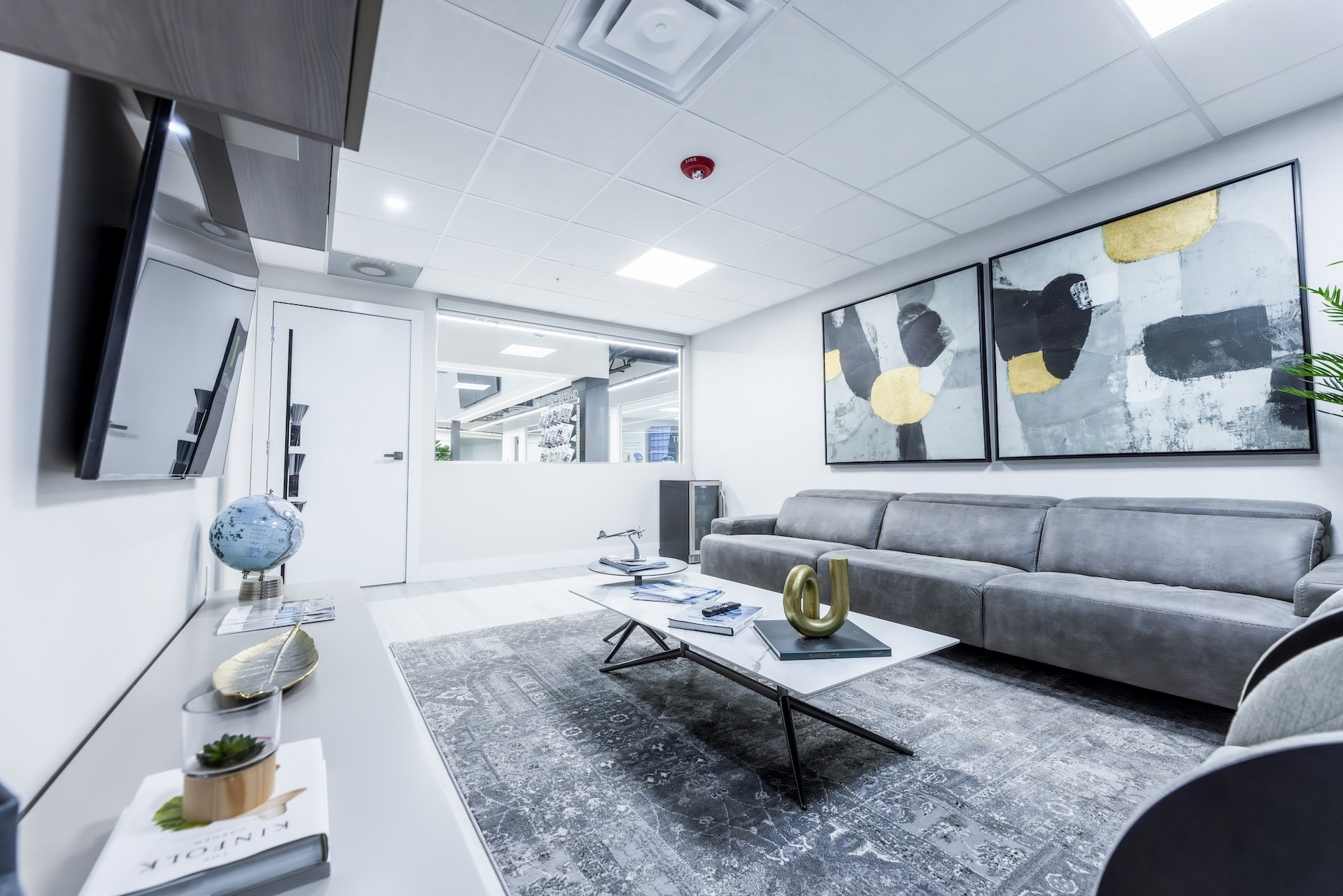 Modern office lounge with gray sofa, abstract paintings, white coffee table, and decorative items like a globe and plant.