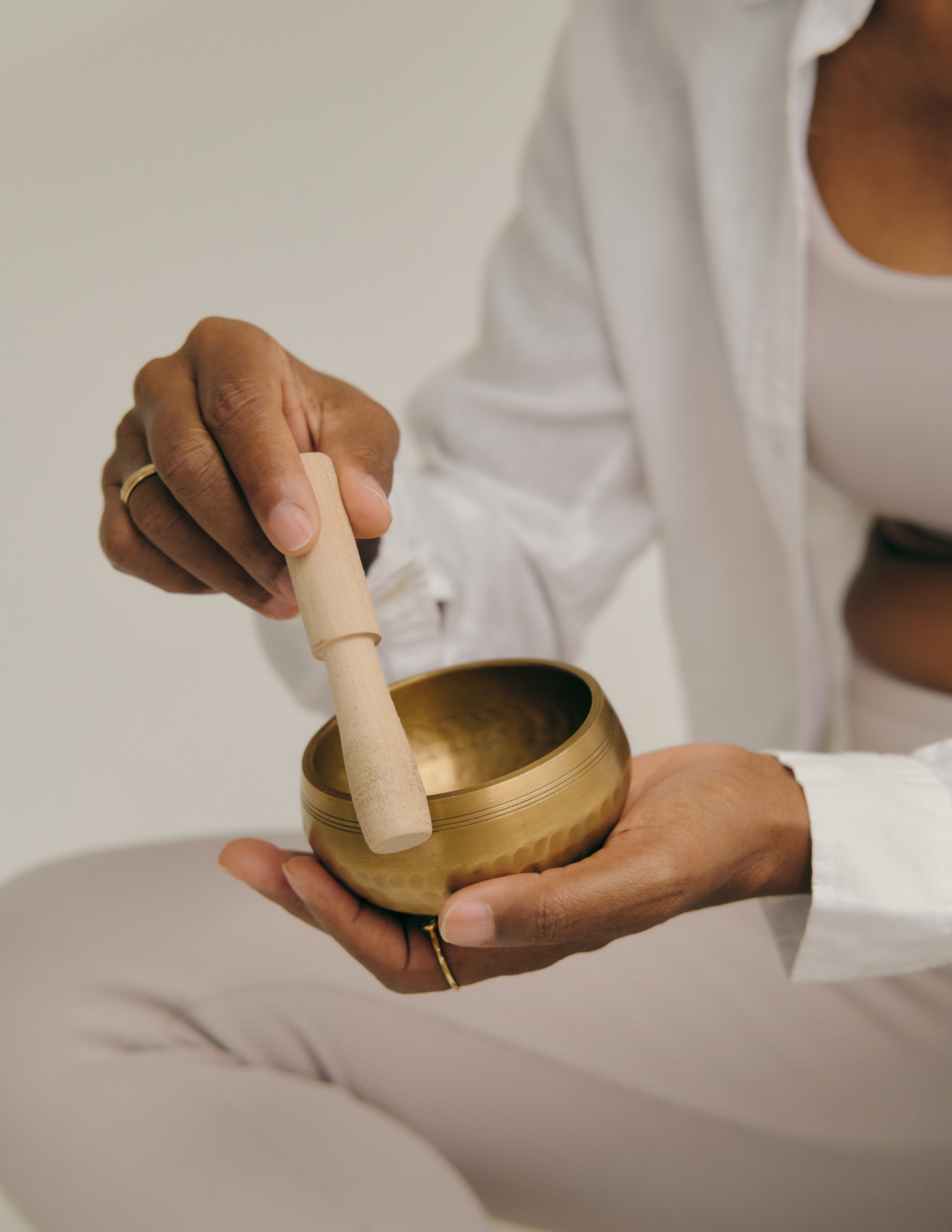 Person holding a brass singing bowl and a wooden mallet, wearing a white outfit.