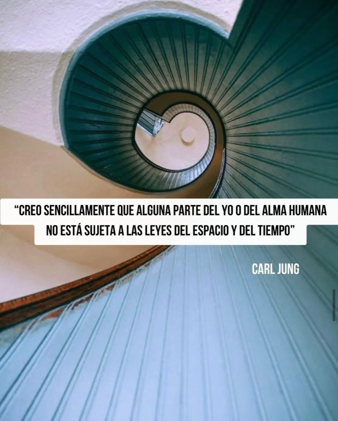 Vista desde arriba de una escalera en espiral con la barandilla y paredes de color beige y azul.