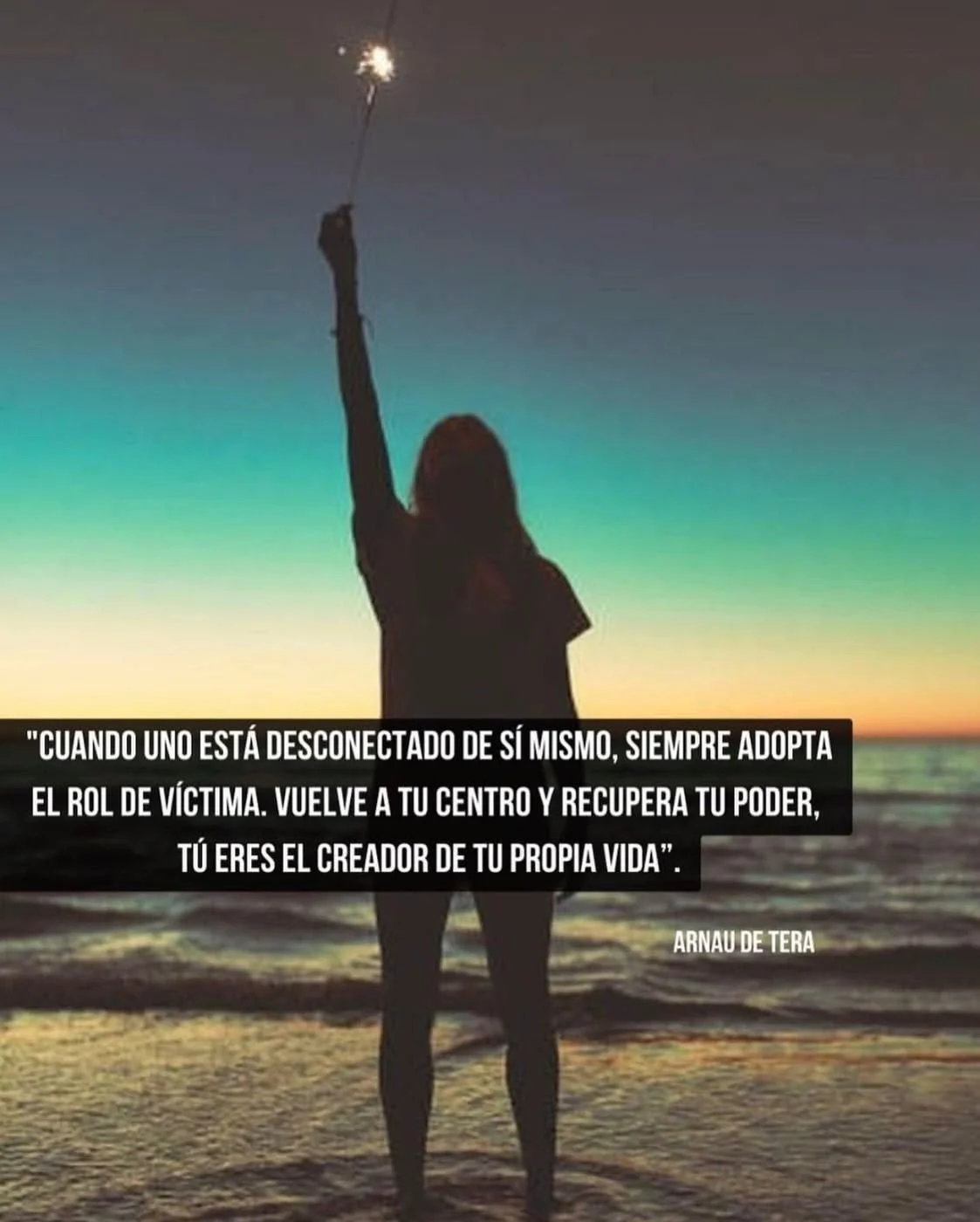 Persona con silueta levantando una vara con una chispa en la playa al atardecer, fondo de cielo con tonos azules, verdes y naranjas.