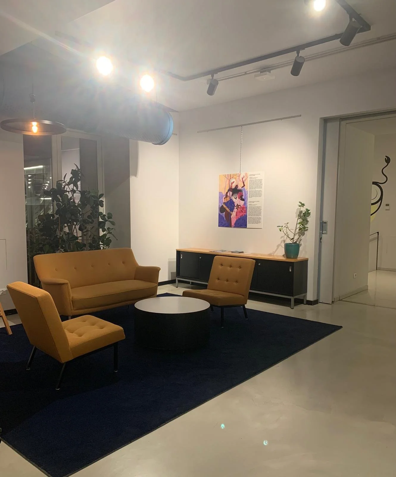 Sala de estar con sillones amarillos, mesa redonda negra, alfombra negra, y una consola con plantas y un cuadro en la pared.