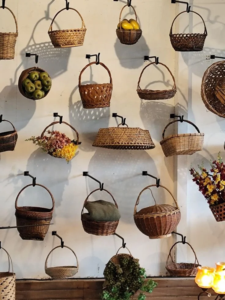 A wall decorated with various woven baskets and some artificial flowers.