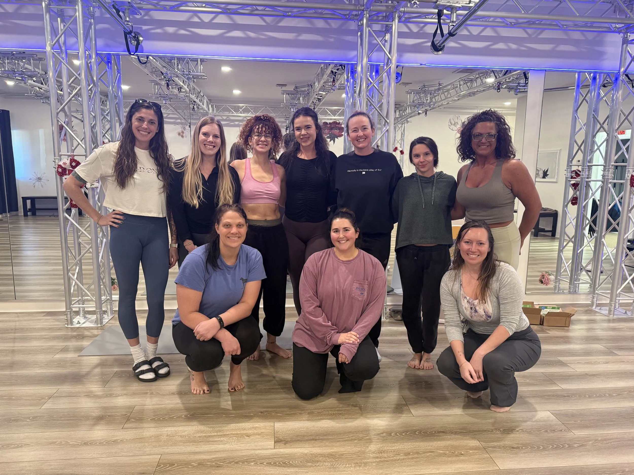 Group of women standing and kneeling on a dance studio floor inside of Wild Ones Fitness Studio following workshop on pelvic floor physical therapy, rehabilitation, and women's health.