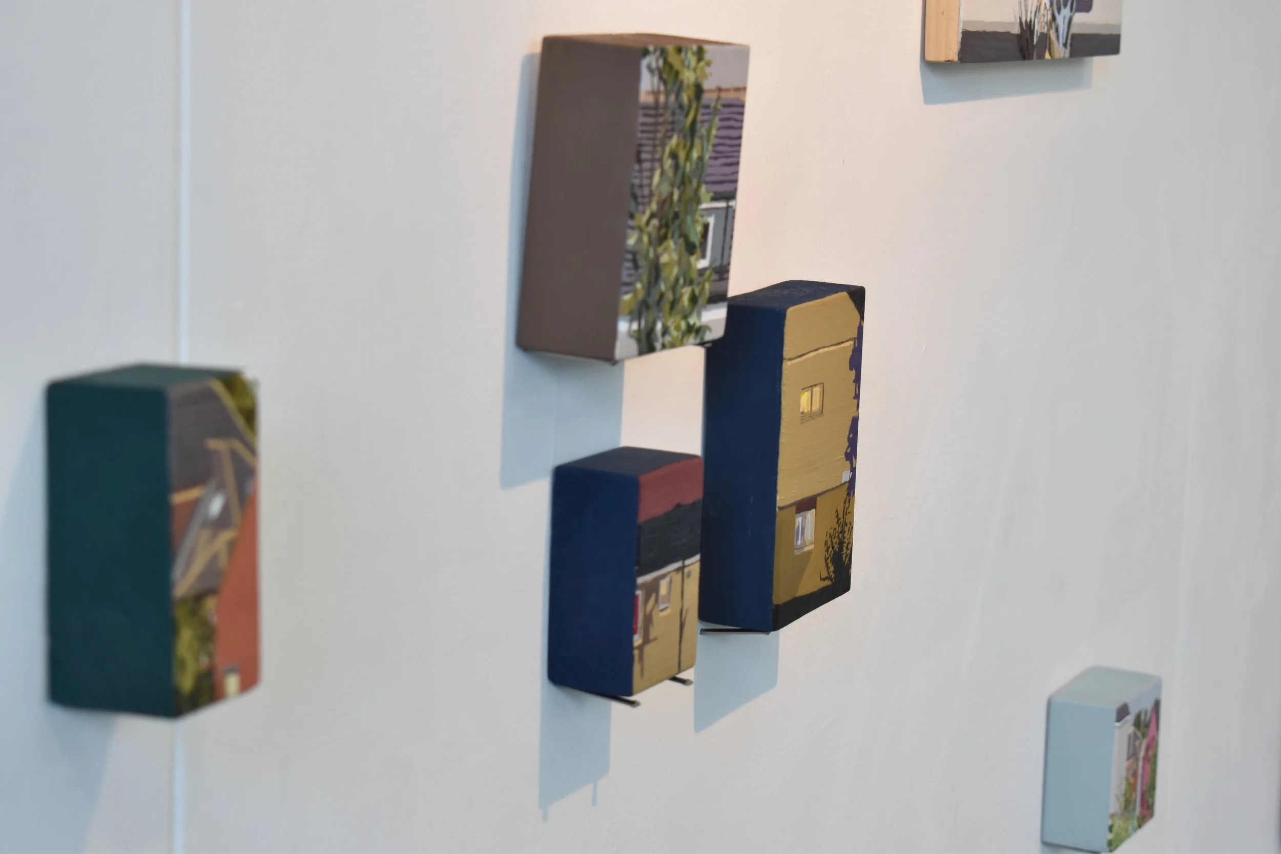 Various small, painted wooden blocks attached to a white wall, depicting different scenes and designs.