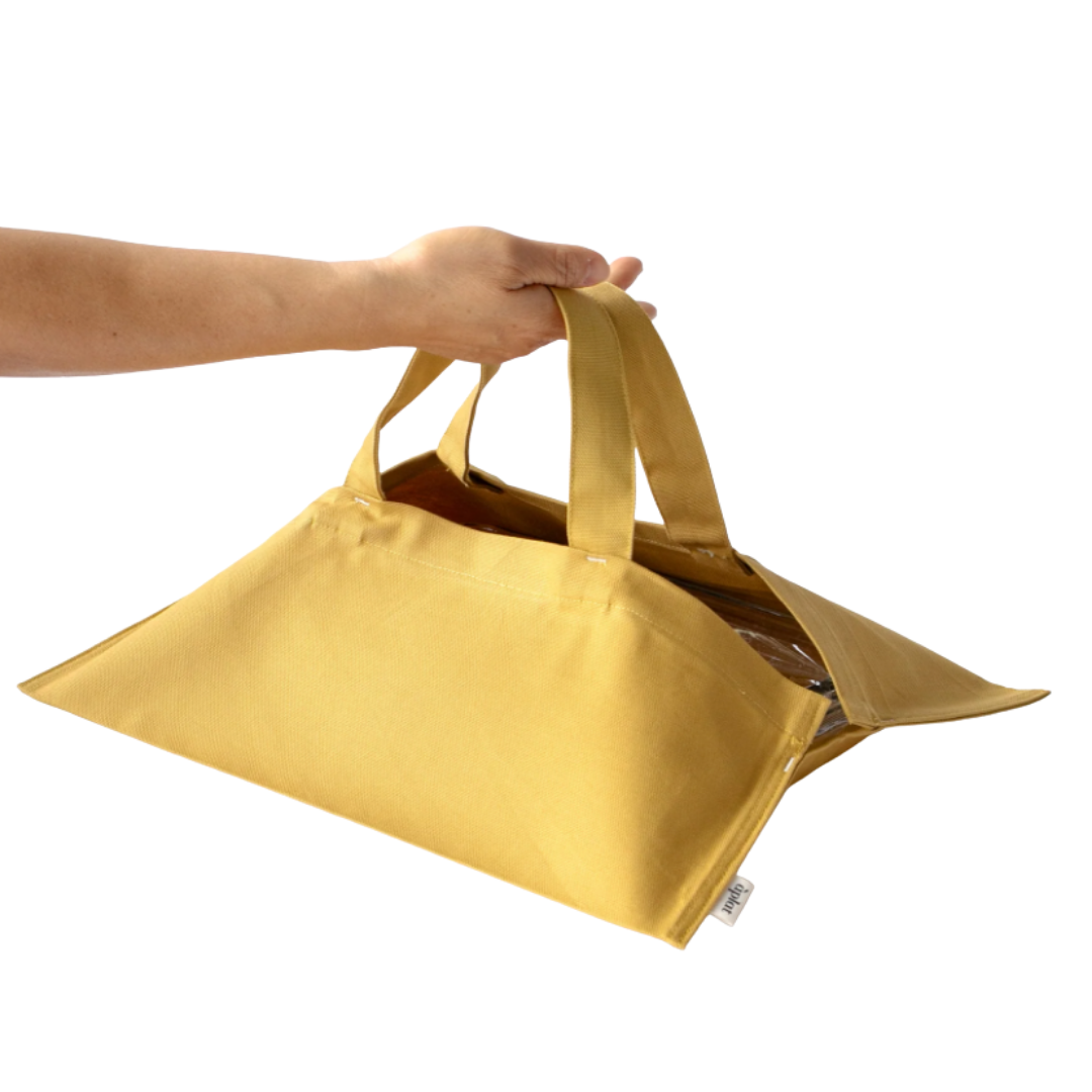 A hand holding a yellow insulated tote bag with handles, partially open, revealing the interior.