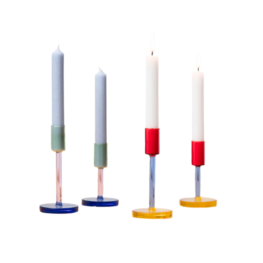 Four lit candles in colorful holders against a white background.