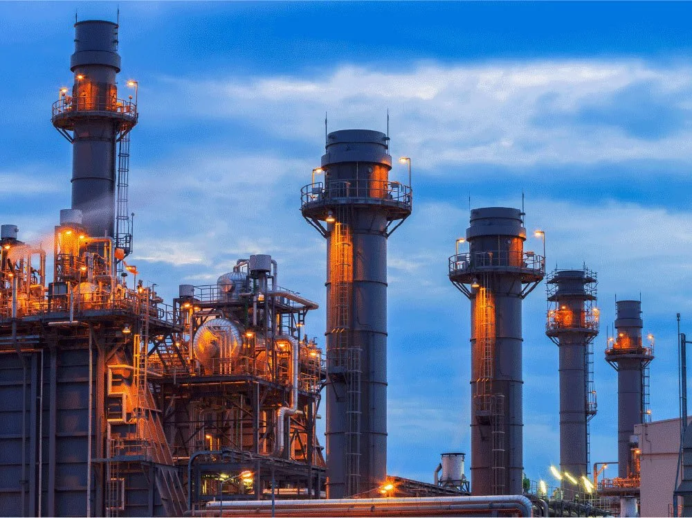 Industrial refinery with tall pipes and metal structures illuminated by orange lights during dusk