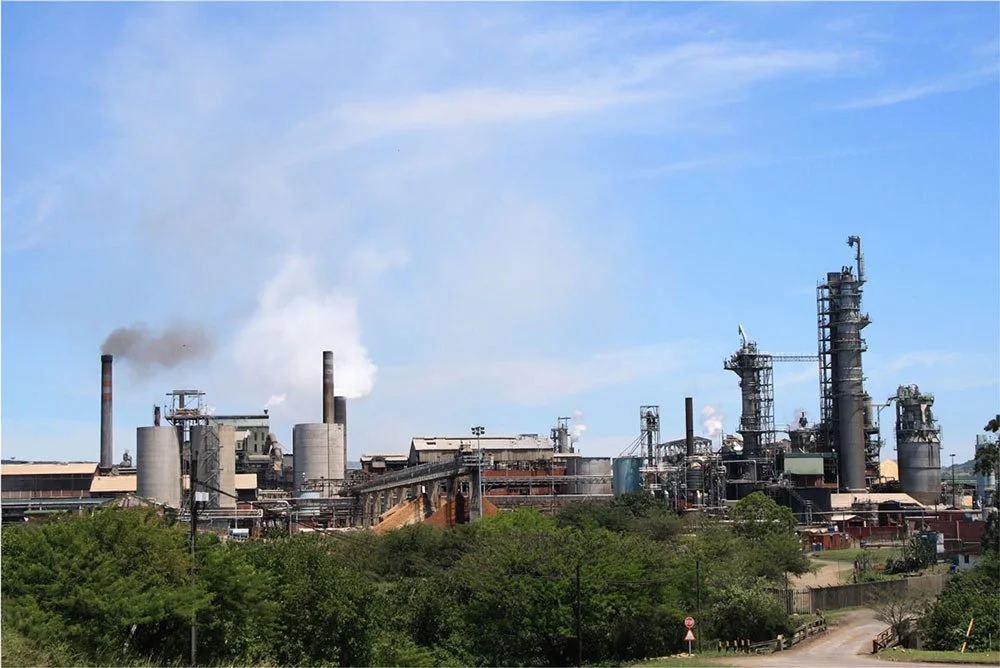 Industrial factory with smokestacks, emitting smoke into the blue sky, surrounded by greenery