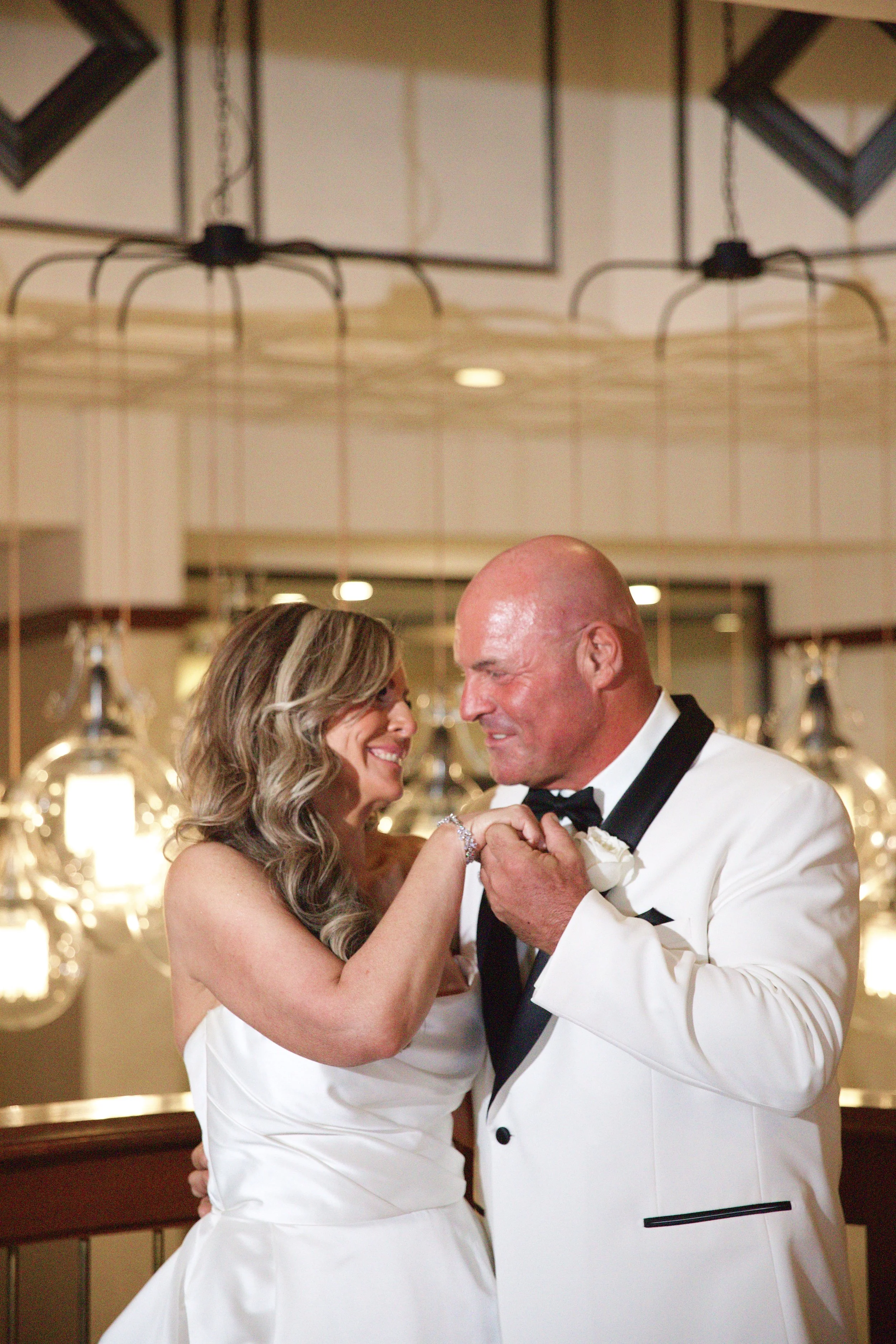 A bride and groom share a dance during their wedding reception, smiling and gazing into each other's eyes.