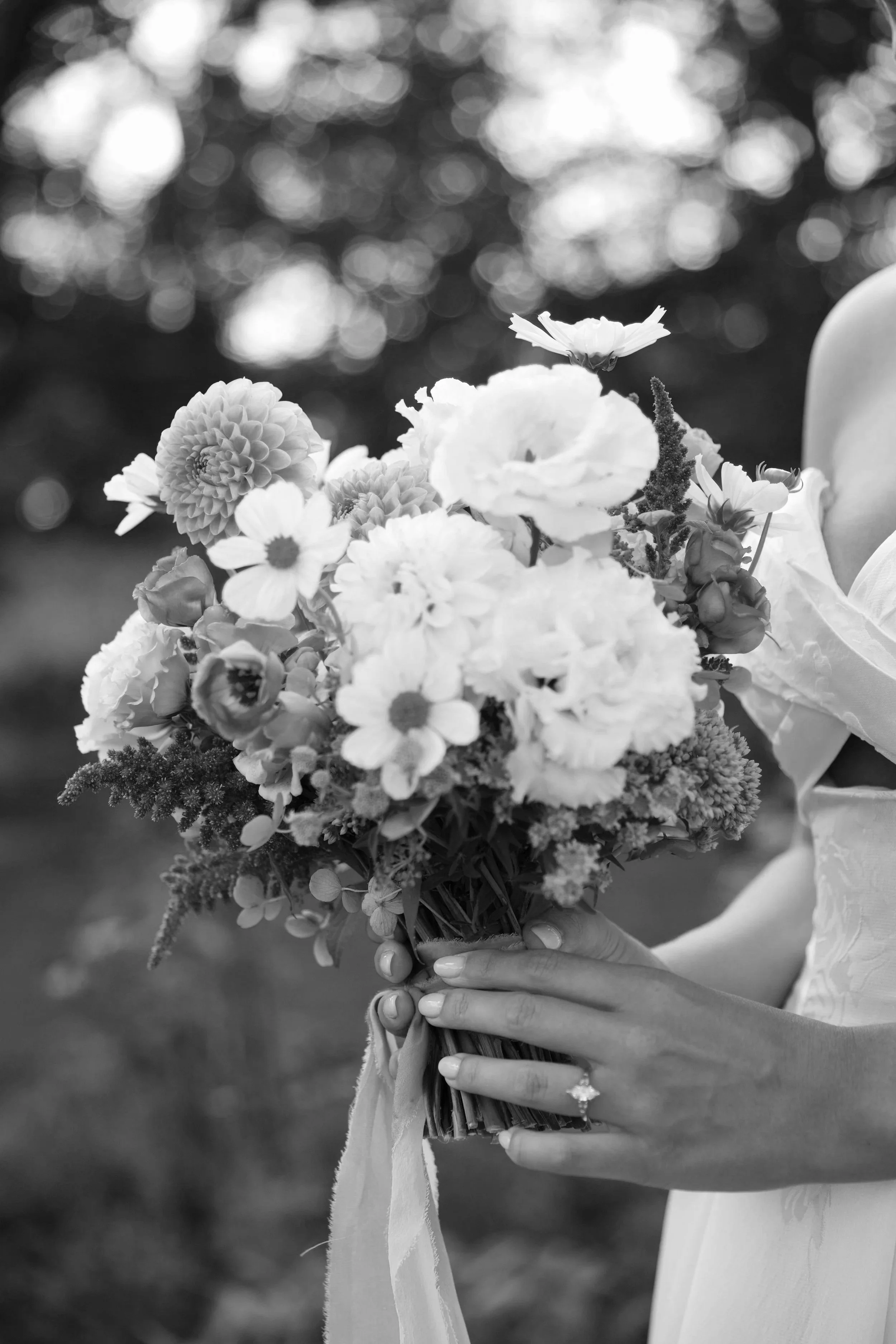 A woman in a wedding dress holding a bouquet of flowers, with her hands clasped around the stems, and a wedding ring visible on her finger.