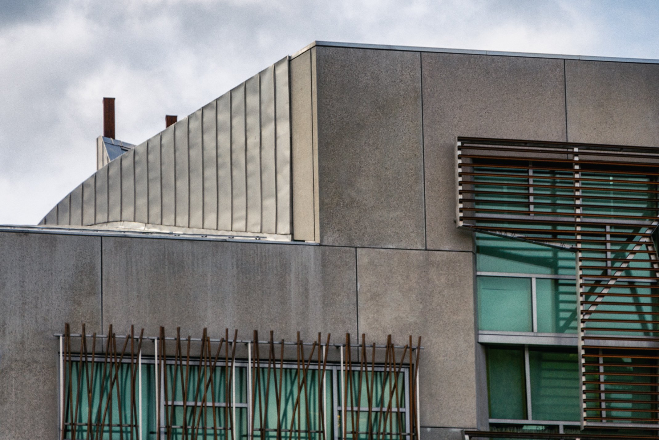 Modern building with concrete and metal exterior, featuring wooden slat window coverings and green-tinted windows.