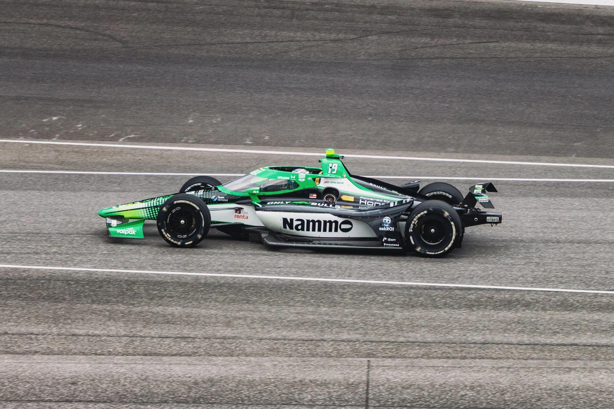 A sleek green and black electric race car with sponsorship logos, racing on a track with a blurred background indicating high speed.