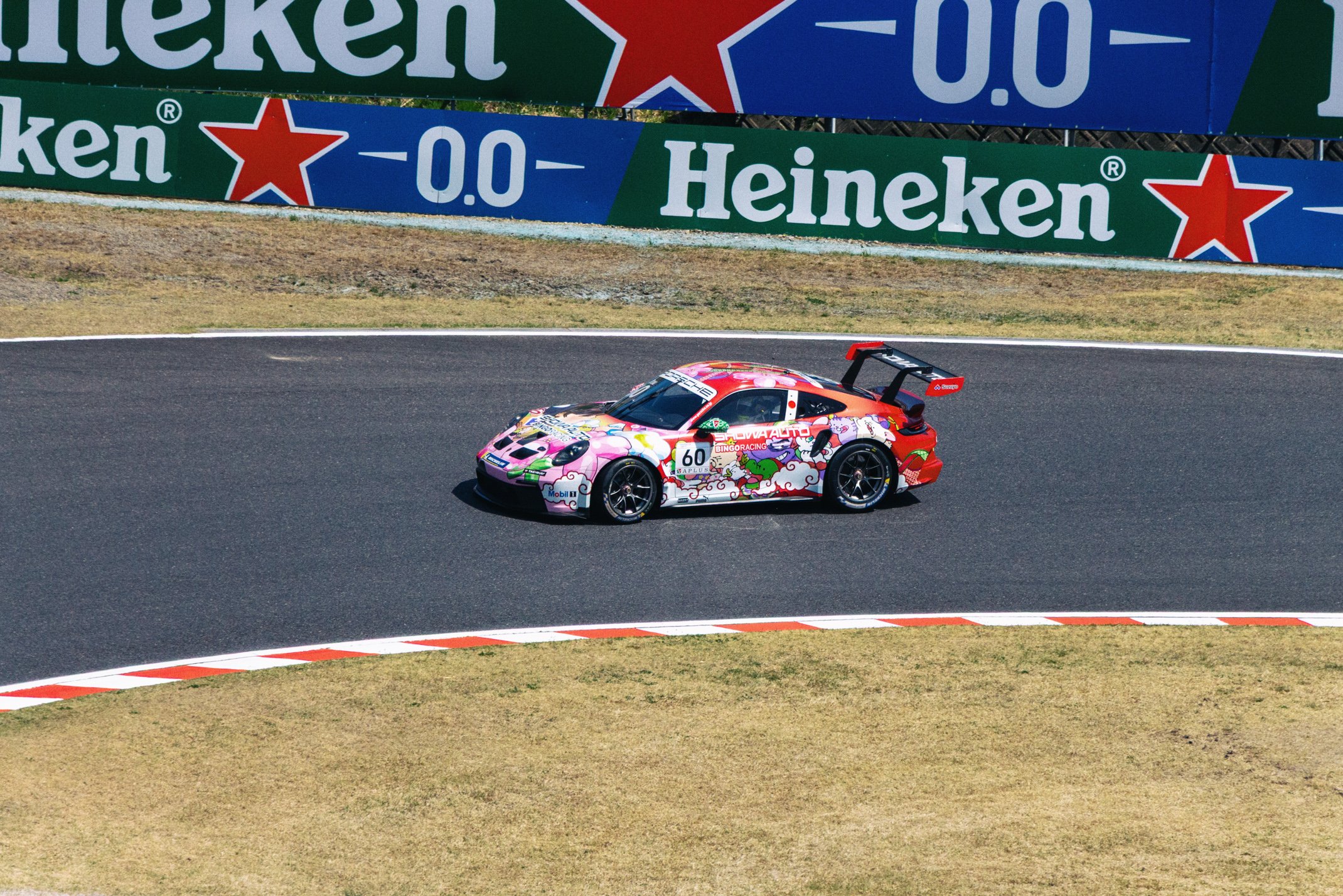 Colorful race car with dragon and cloud graphics on a track, advertising banners in the background