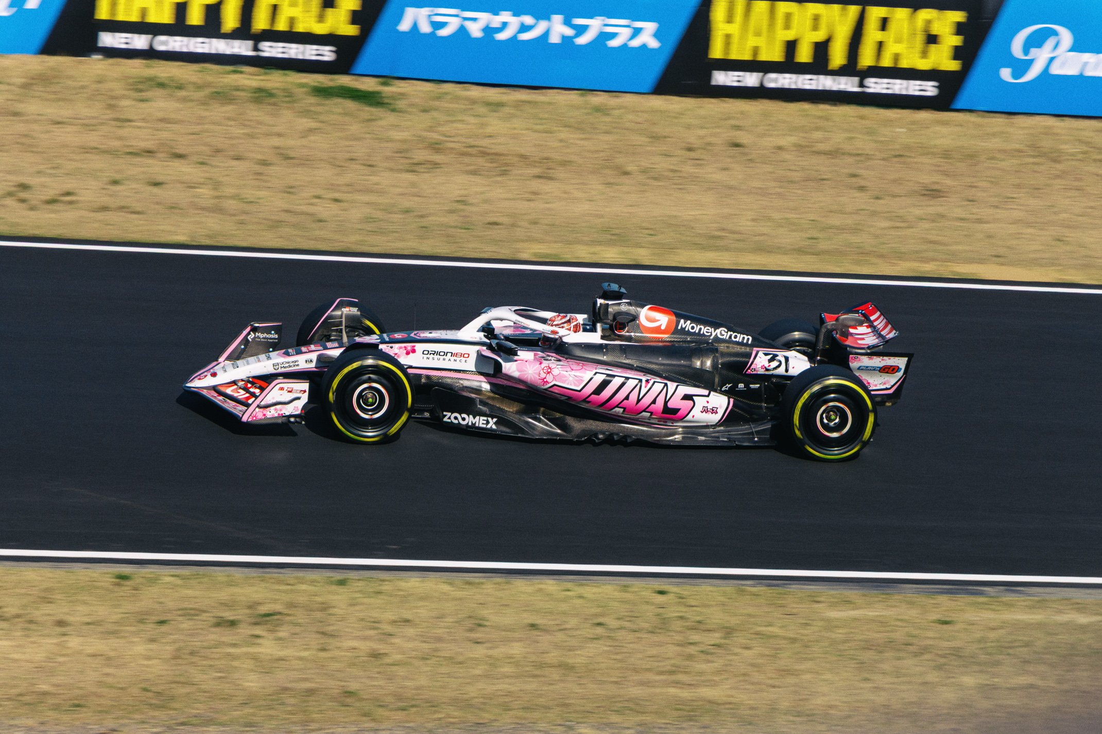 A race car on a track with pink, black, and white livery, featuring sponsorships from JinS, MoneyGram, and other brands.