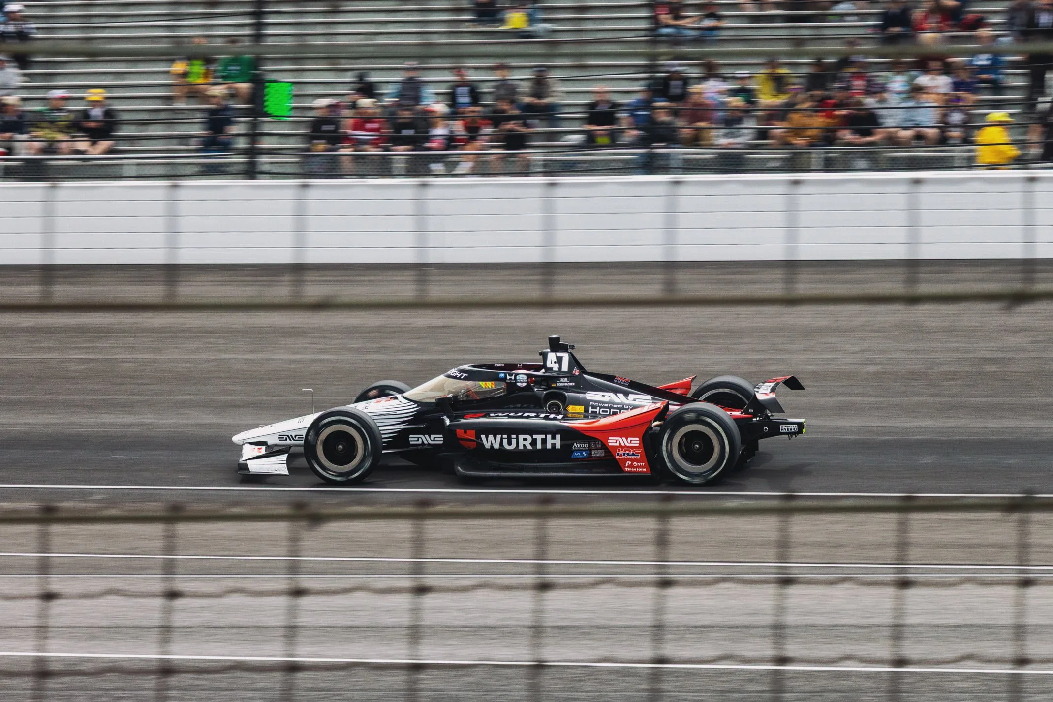 Race car speeding on track with spectators in the background.