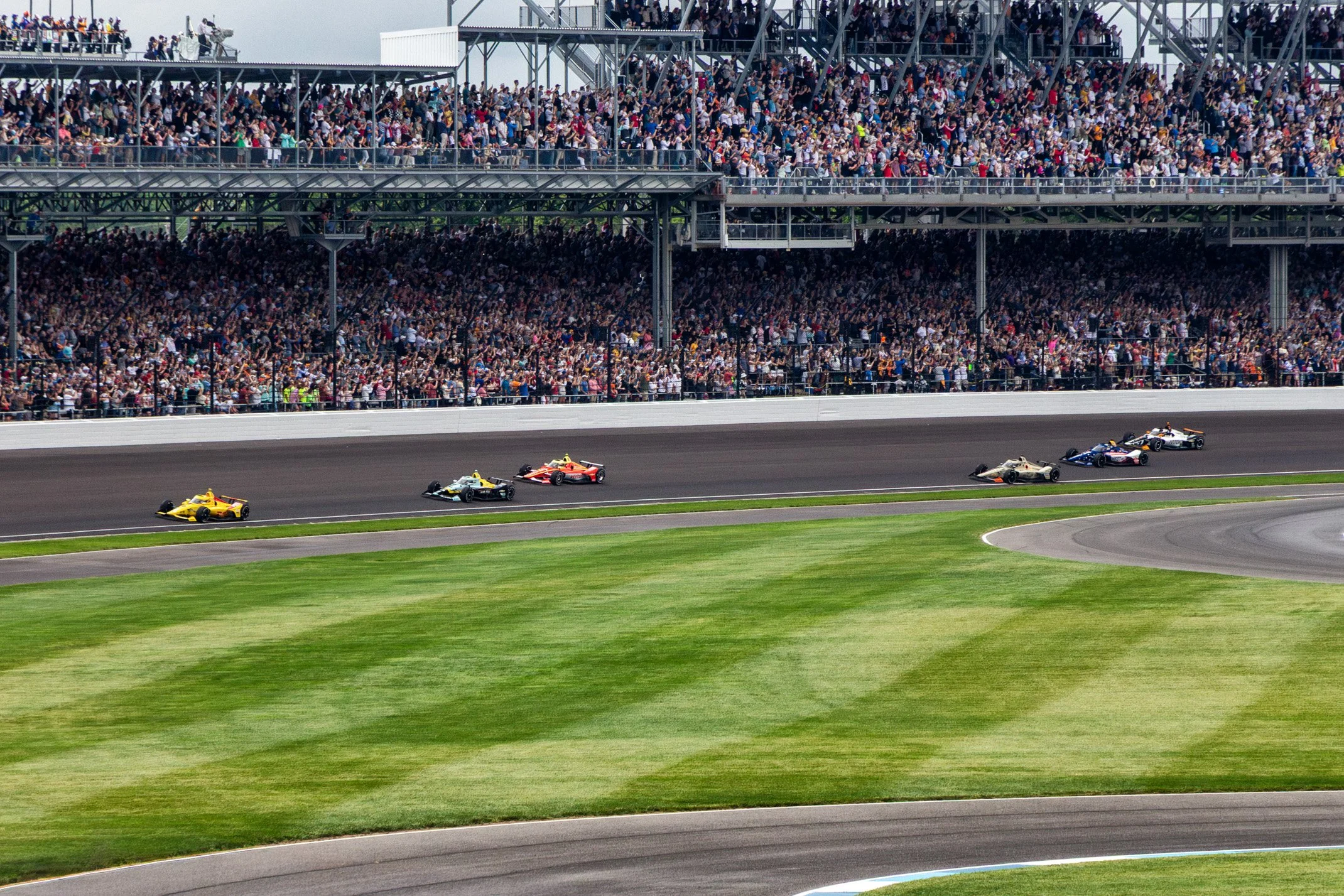 Race cars on a track with a crowded grandstand in the background.