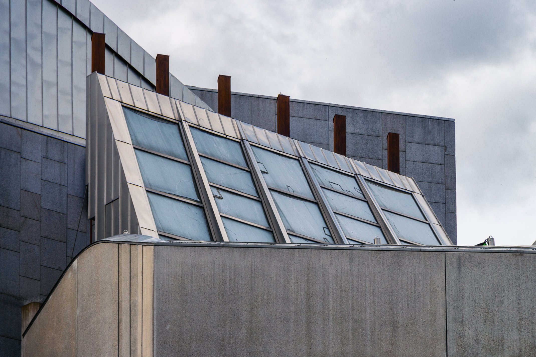 Close-up of modern building with angled glass windows and gray concrete walls under cloudy sky.