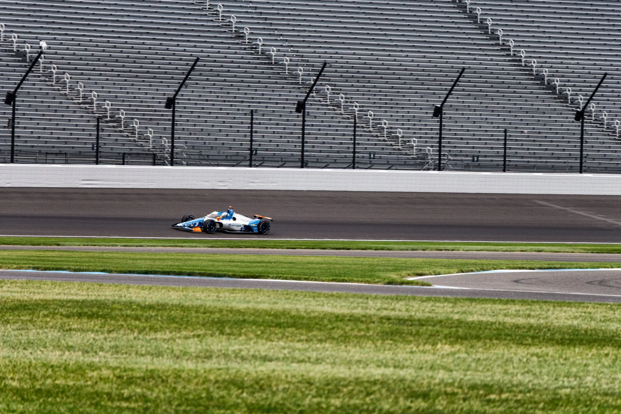 Race car on a racetrack with empty grandstands in the background.
