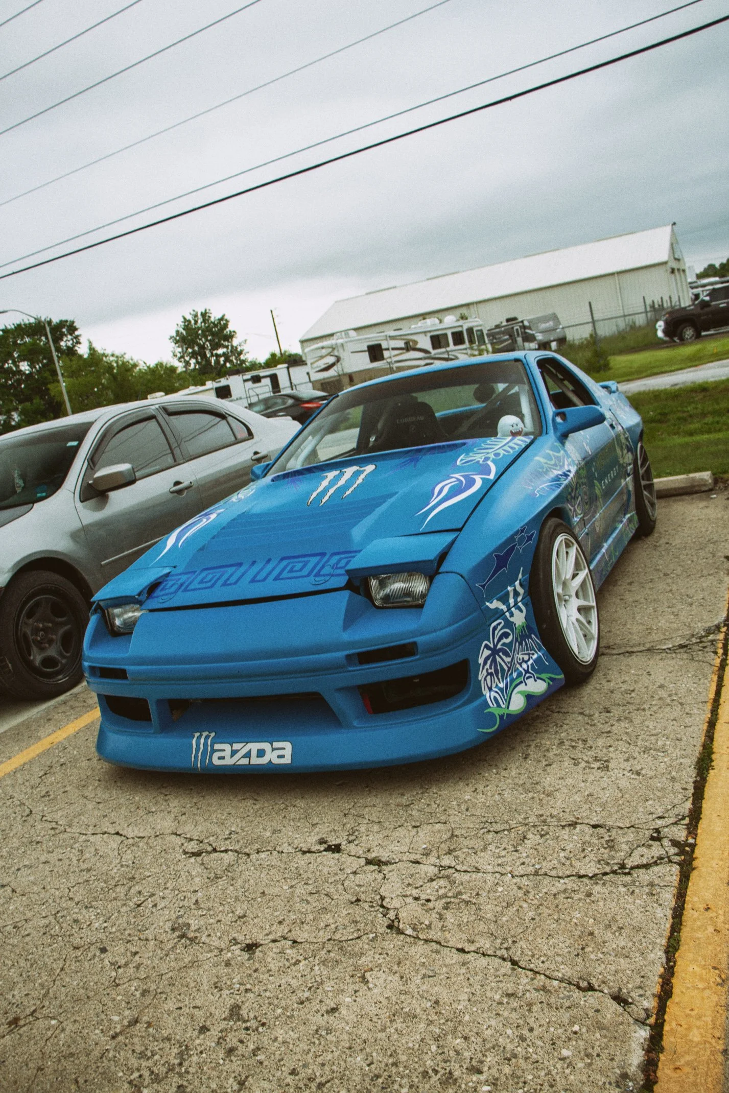 Blue Mazda sports car with Monster energy branding and graphics parked in a parking lot.