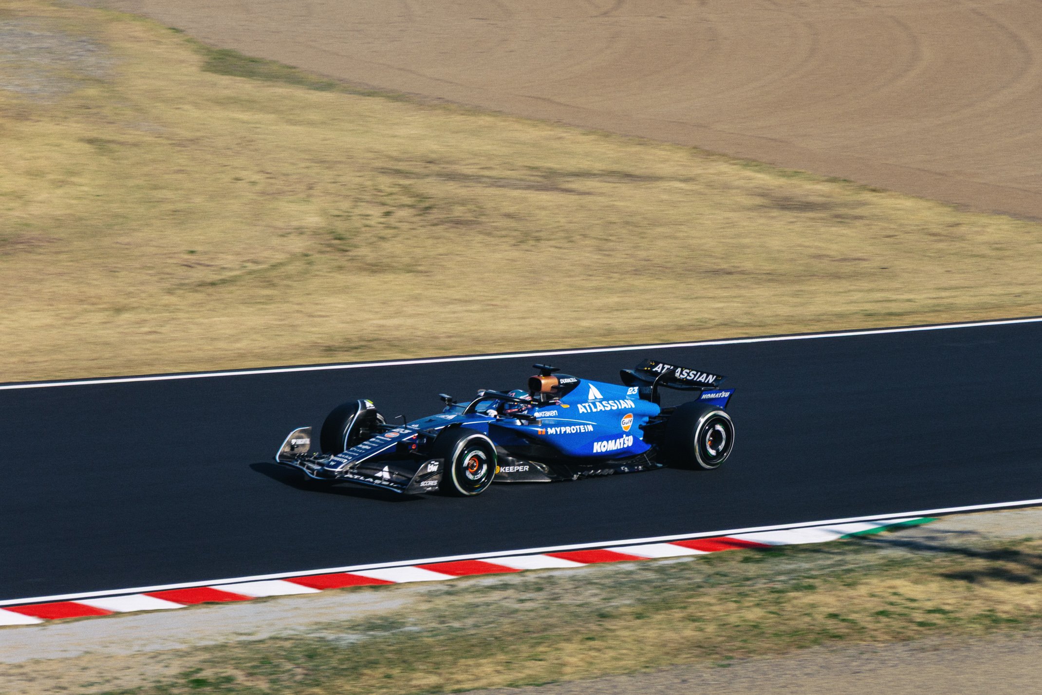 Blue Formula 1 race car on track with sponsor logos including Atlasian and Komatsu