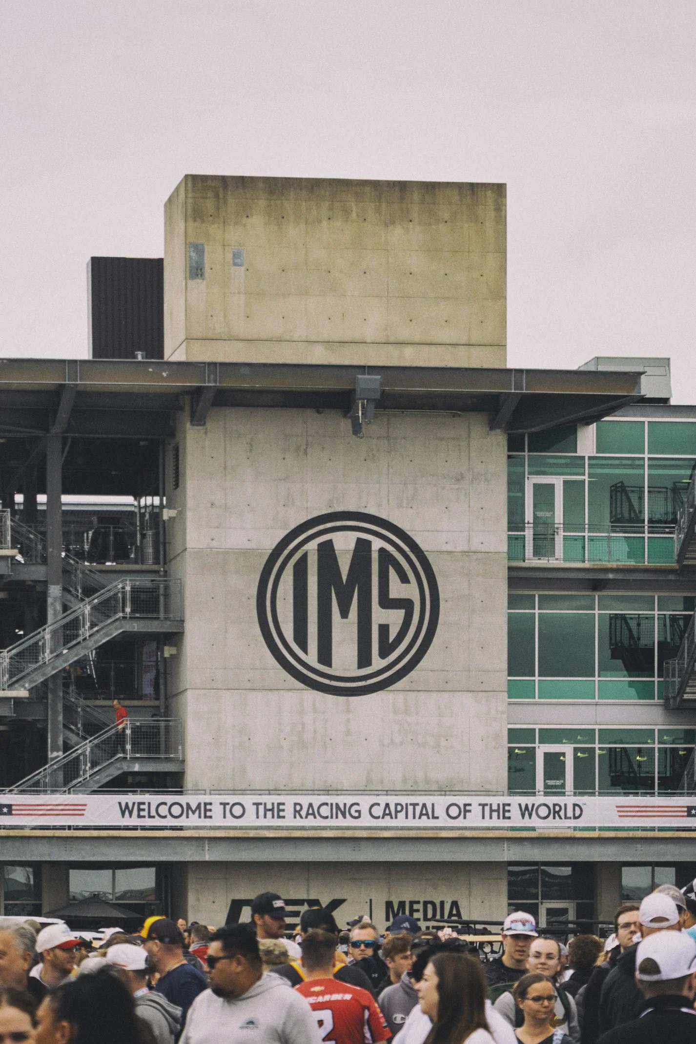 Crowd of people at a racing event with a large building featuring a racing logo and a welcoming banner.