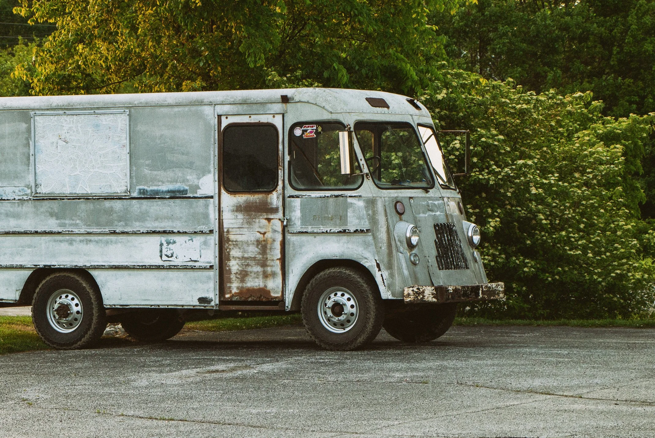 An old, rusty Food Truck parked on a street with a background of green trees and blue sky.