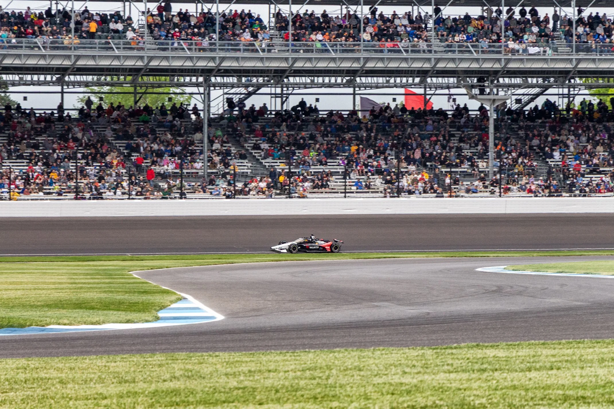 Race car on a race track during a race, with grandstands filled with spectators behind a fence.