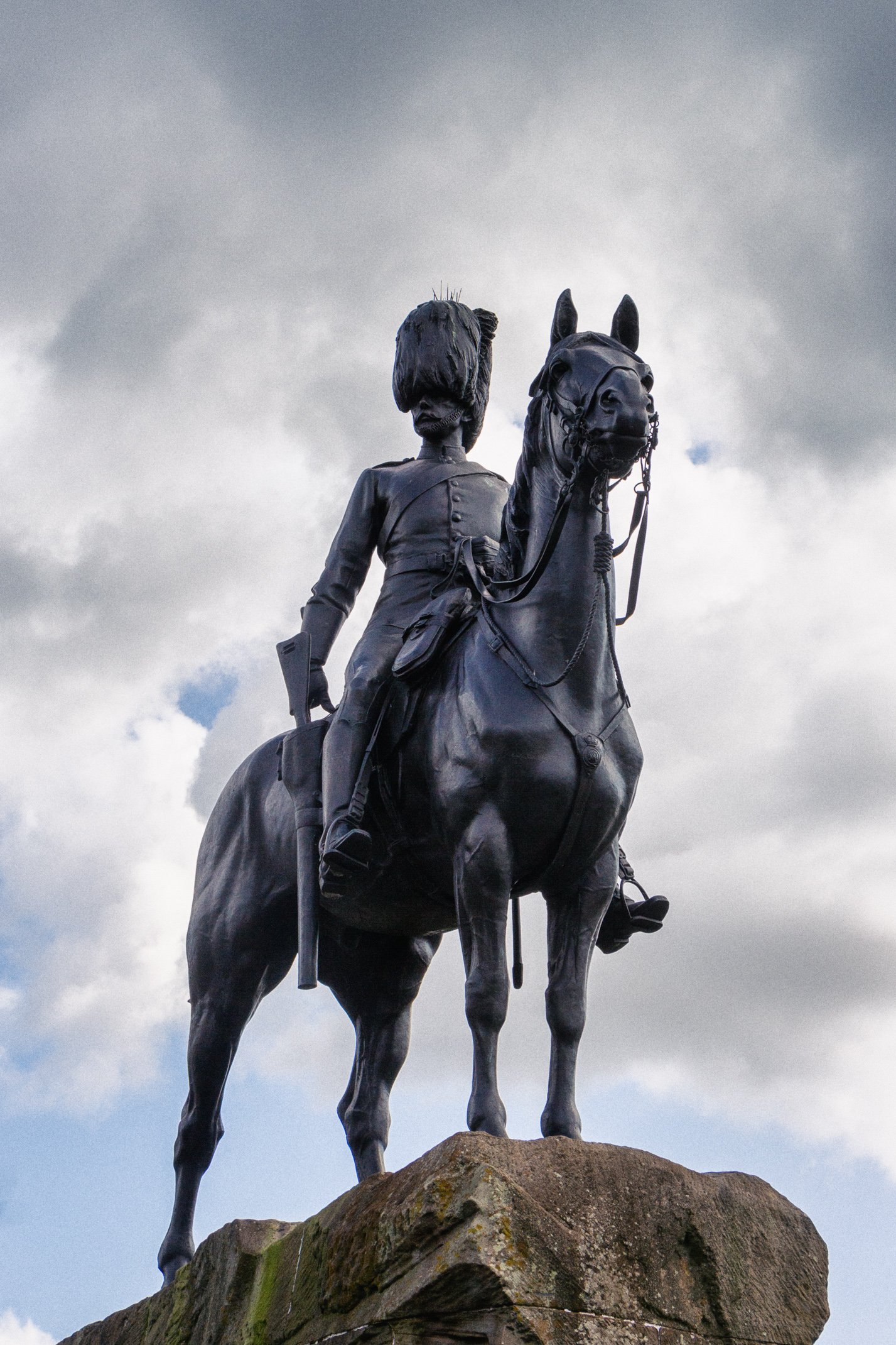 Bronze statue of a soldier on horseback against a cloudy sky, mounted on a large stone pedestal.