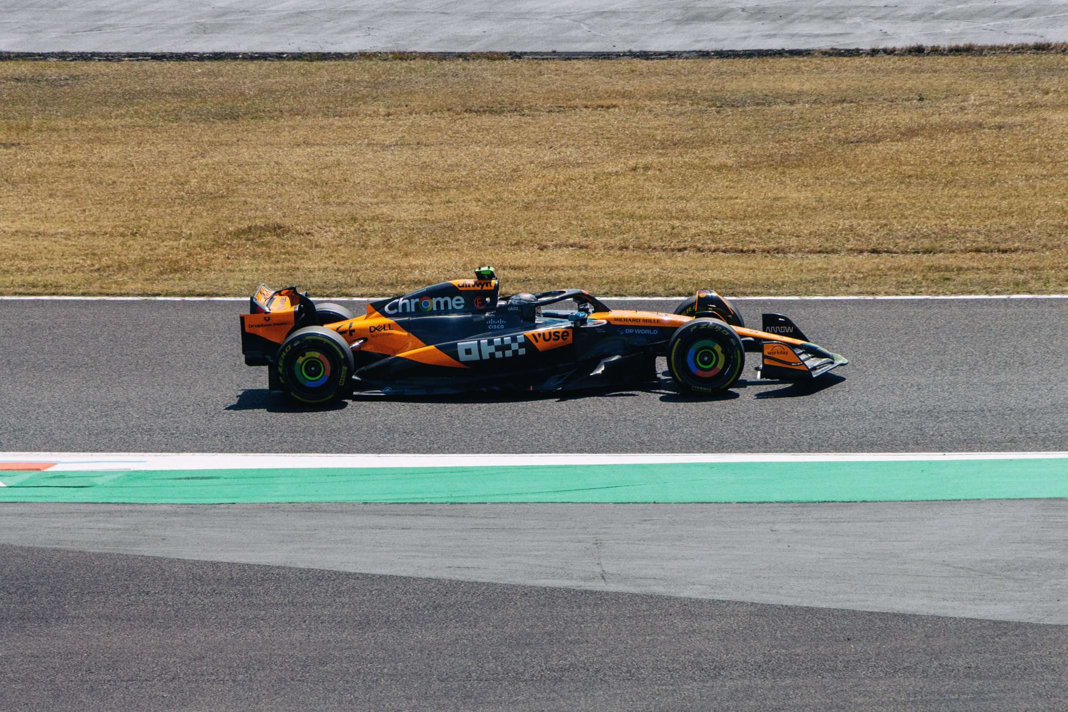 A sleek race car with a black and orange livery driving on a race track.