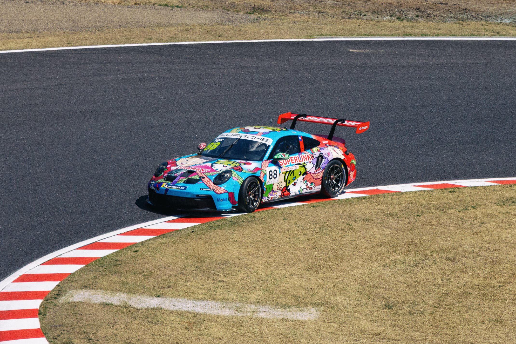 A race car with a colorful, cartoon-themed livery speeding on a race track, navigating a turn.