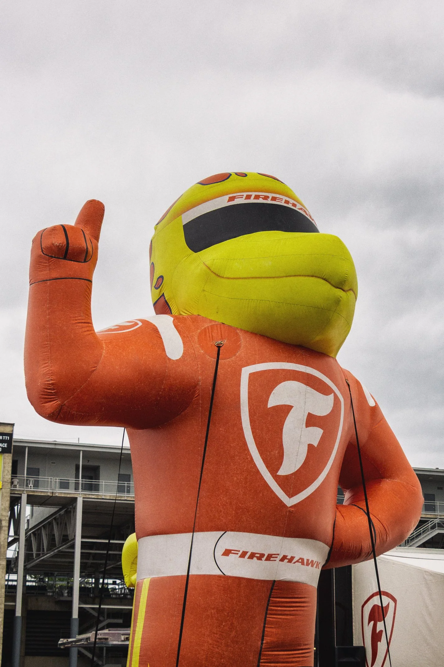 A large inflatable mascot for FireHawk, a barbecue restaurant, resembling a firefighter with a duck's face, yellow helmet, and orange suit, raising its right hand with one finger pointing upward.
