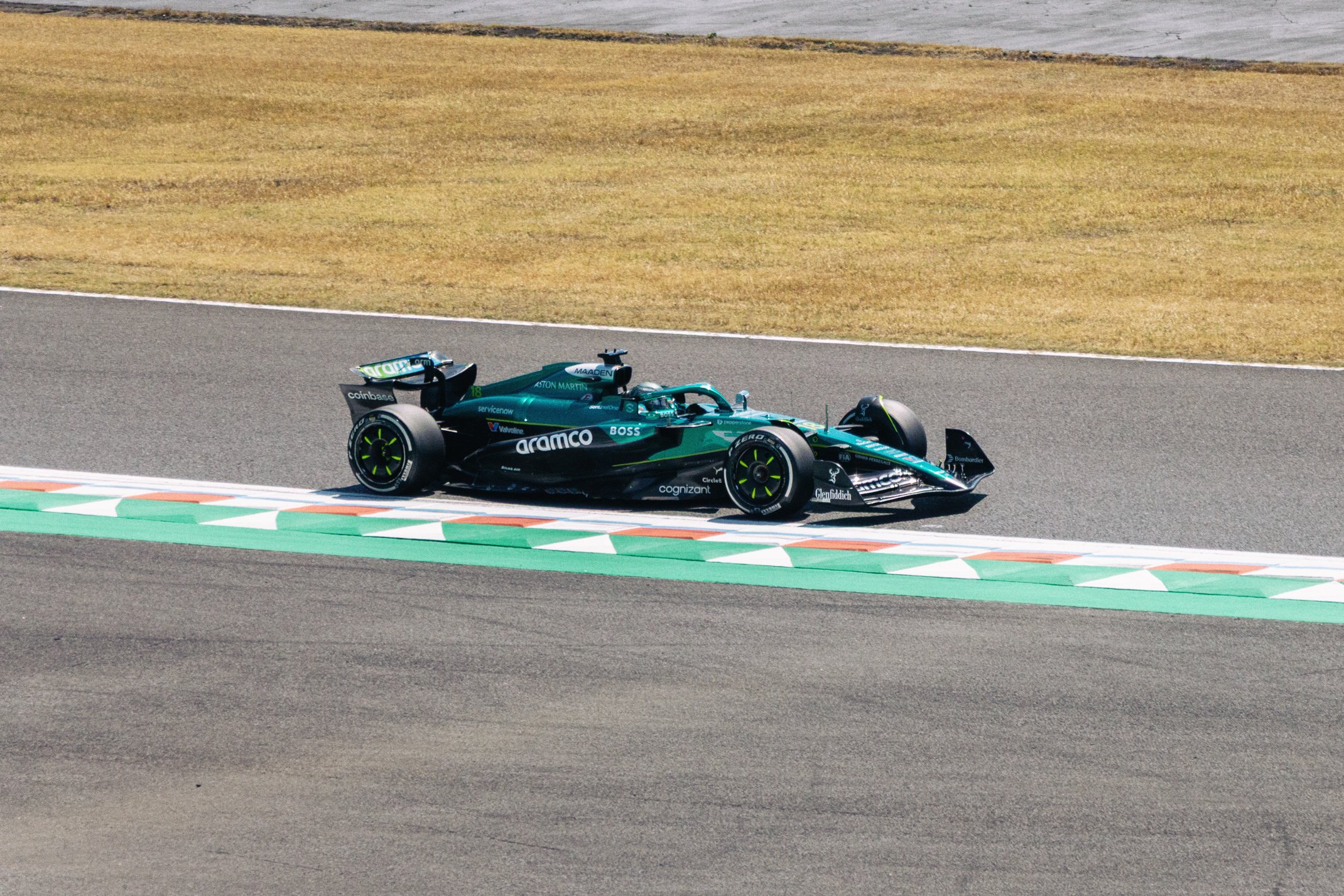 A blue racing car on a track with colorful curbs, next to grassy areas and distant pavement.