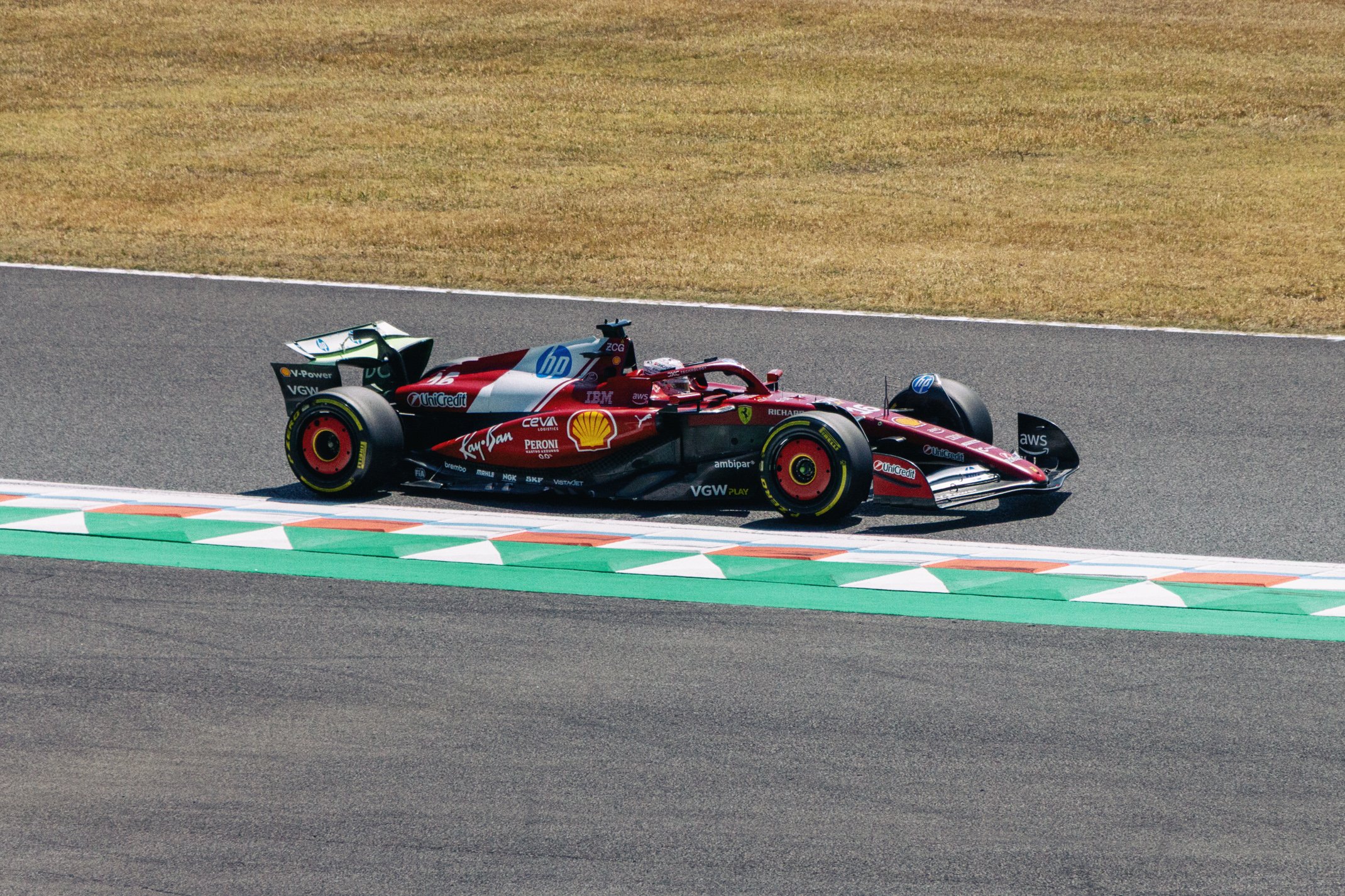 A red racing car driving on a race track near the curbing with grass in the background.