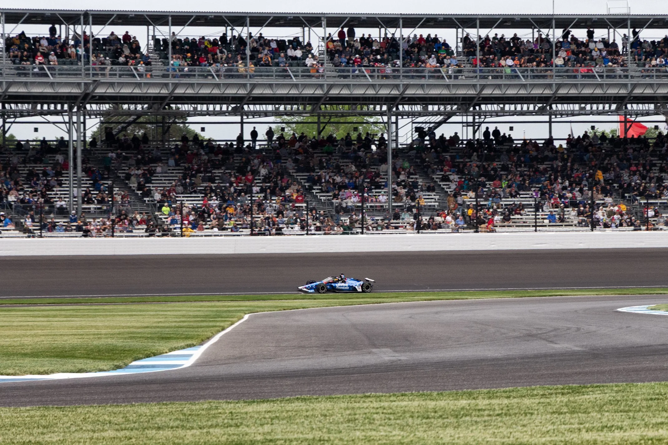 Race car speeding around a track with grandstands filled with spectators in the background.