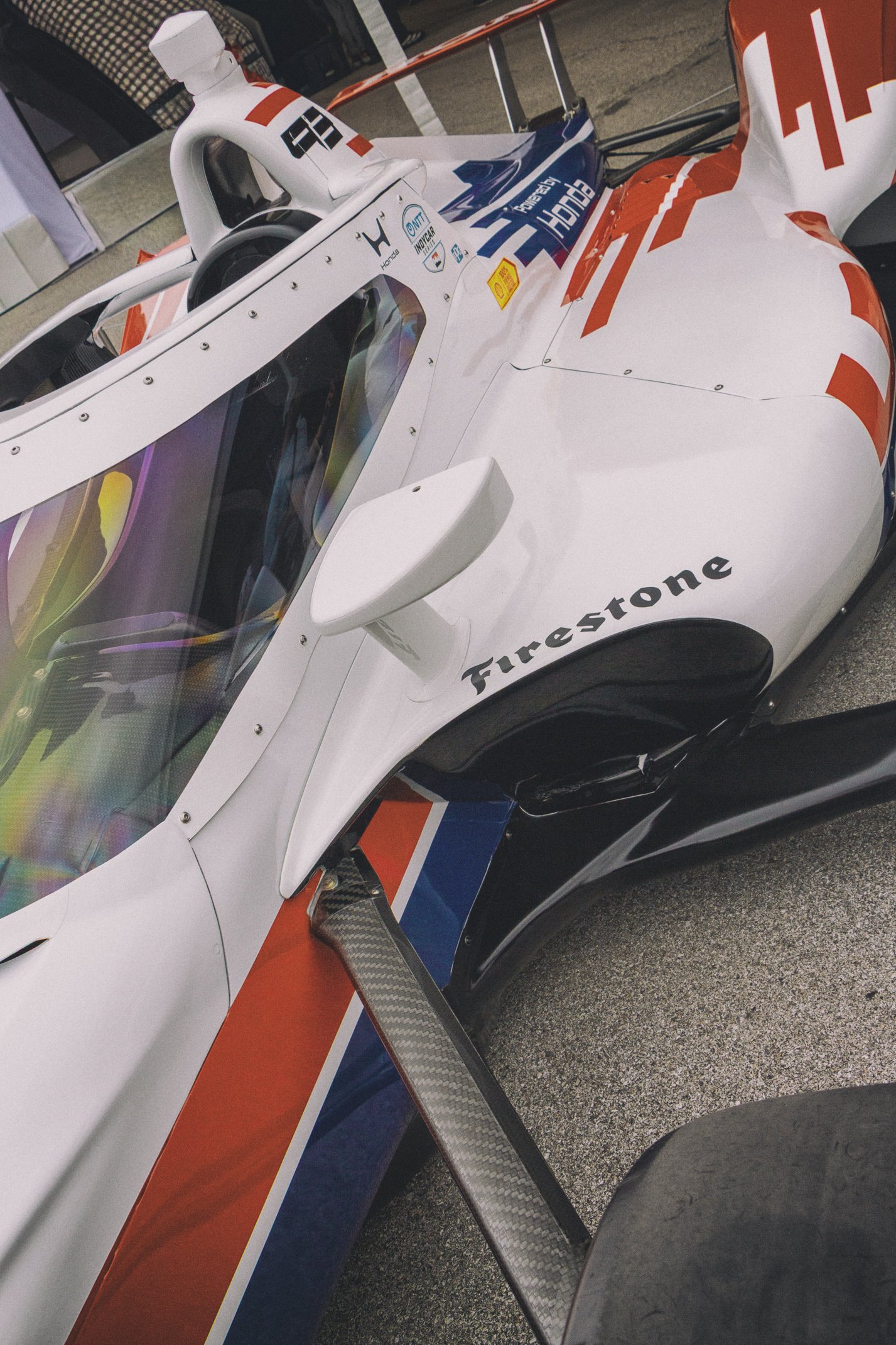 A race car with a sleek, aerodynamic design, painted in white with red and blue accents, featuring sponsorship stickers, a large rear wing, and a cockpit with a tinted windshield.