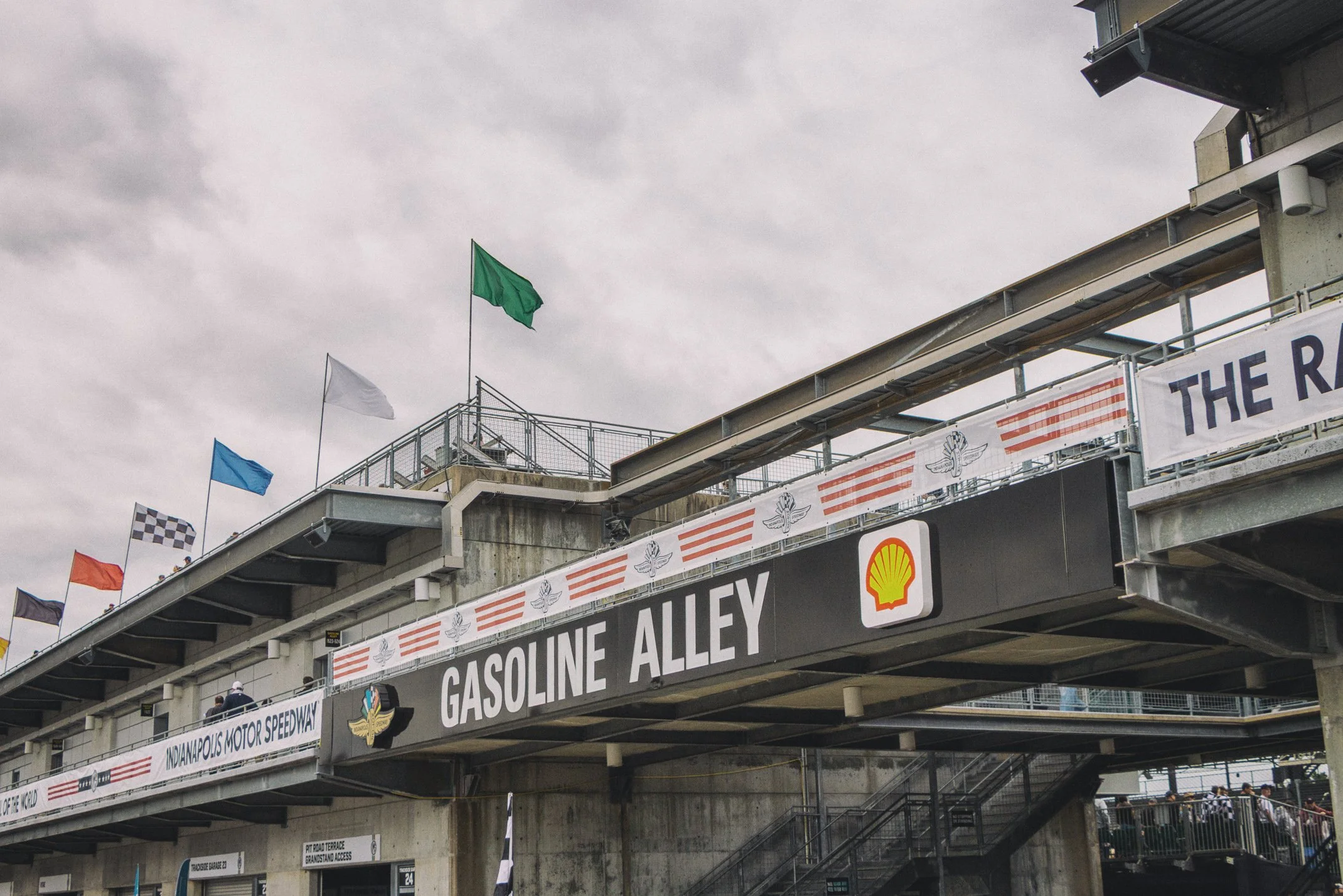 View of the grandstand at Indianapolis Motor Speedway with flags flying and banners displaying the track's name and sponsors.