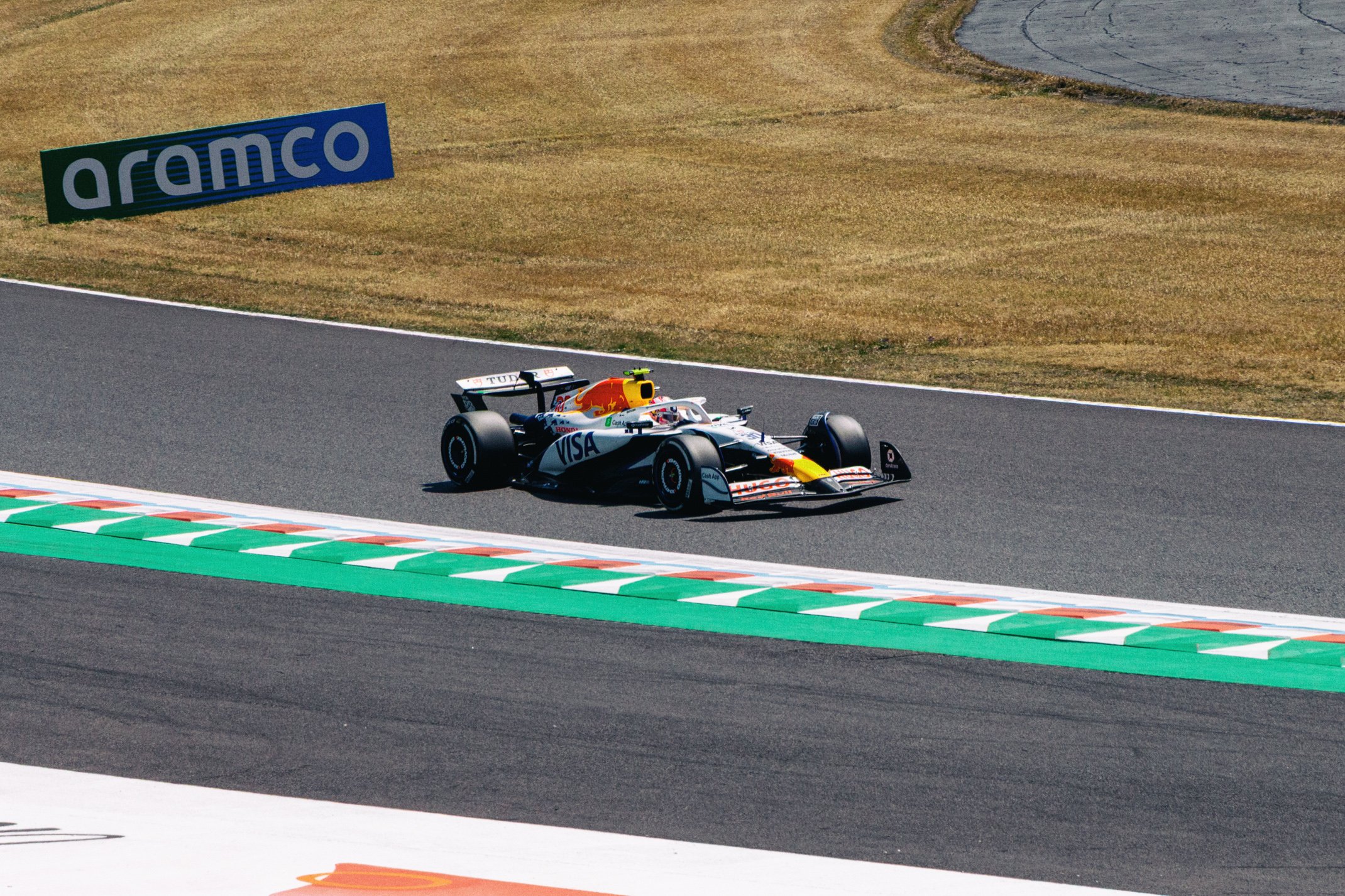 A Formula 1 race car on a track with a green, white, and red painted curb, and a grassy background with a large blue and green Aramco sign.