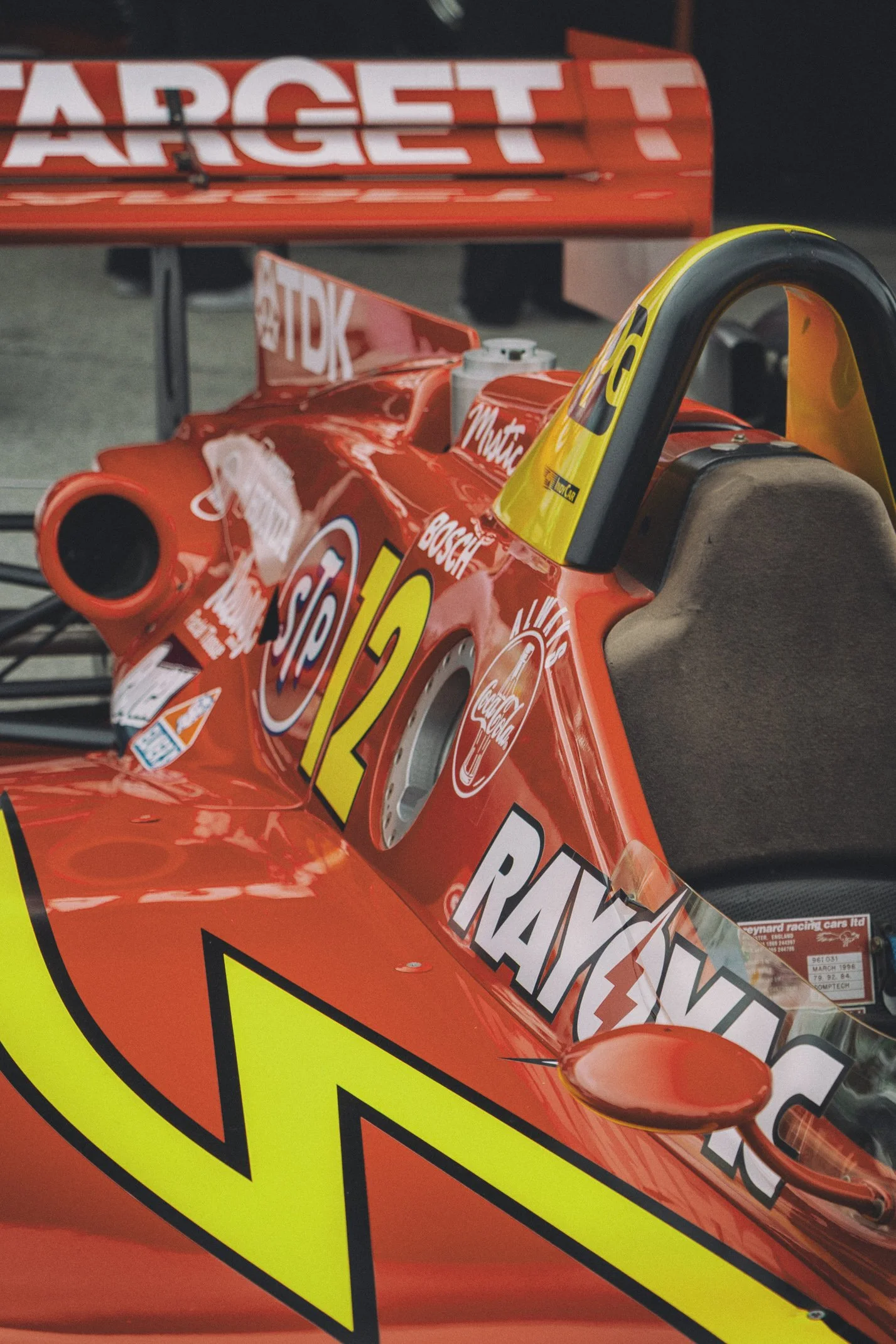 A vintage Marlboro racing car model in red with sponsors' logos, featuring a yellow rear wing and a side mirror, displayed on a stand.