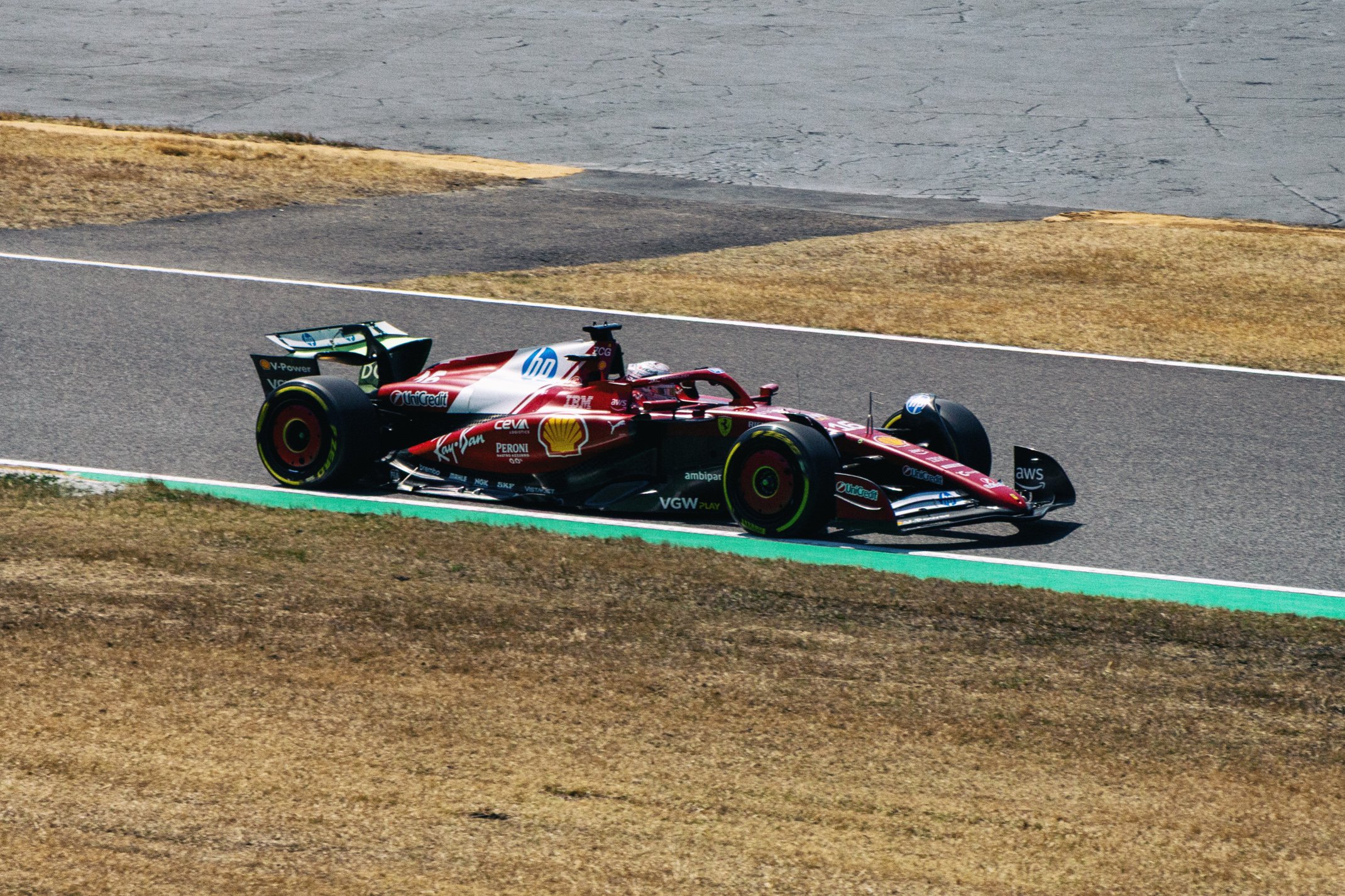 A red Formula 1 race car driving on a race track with dry grass and asphalt