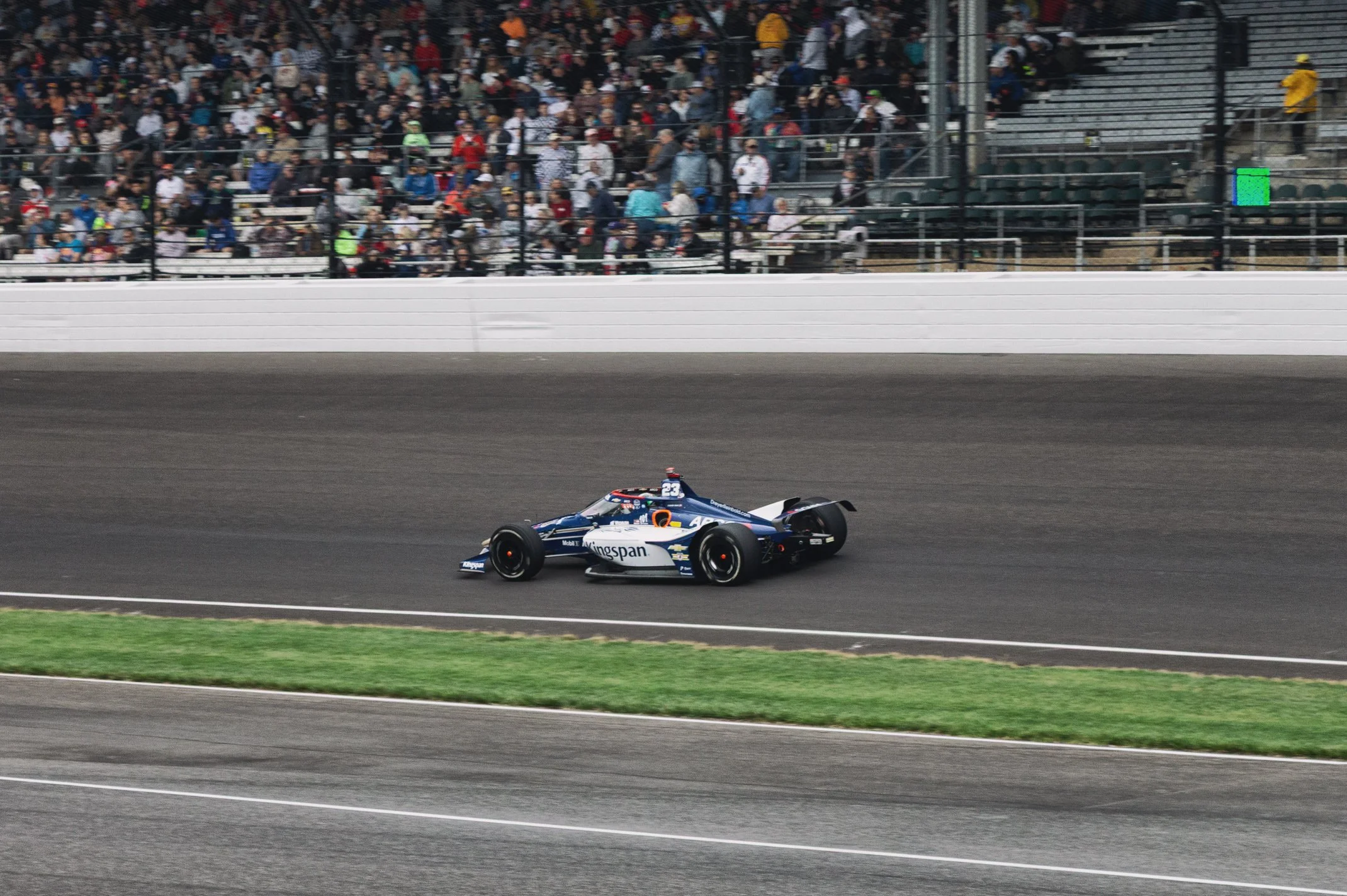 A race car on a track during a motorsport event with a large crowd in the stands.