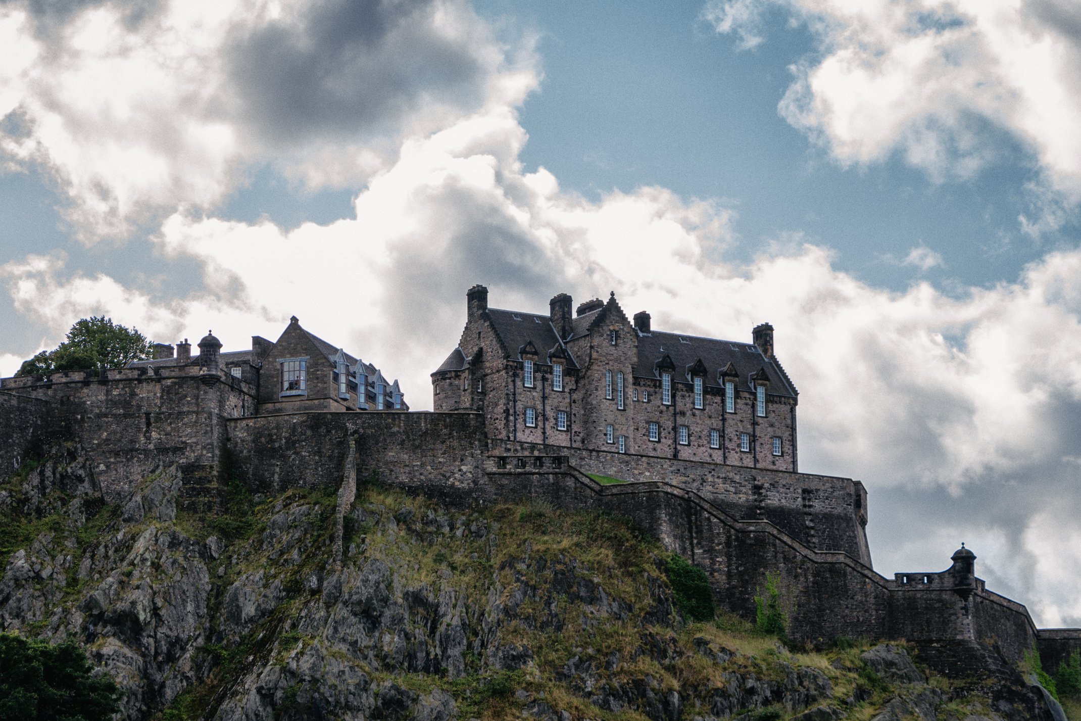A castle on a hill with stone walls and multiple towers, overlooking a rocky landscape, under a cloudy sky.
