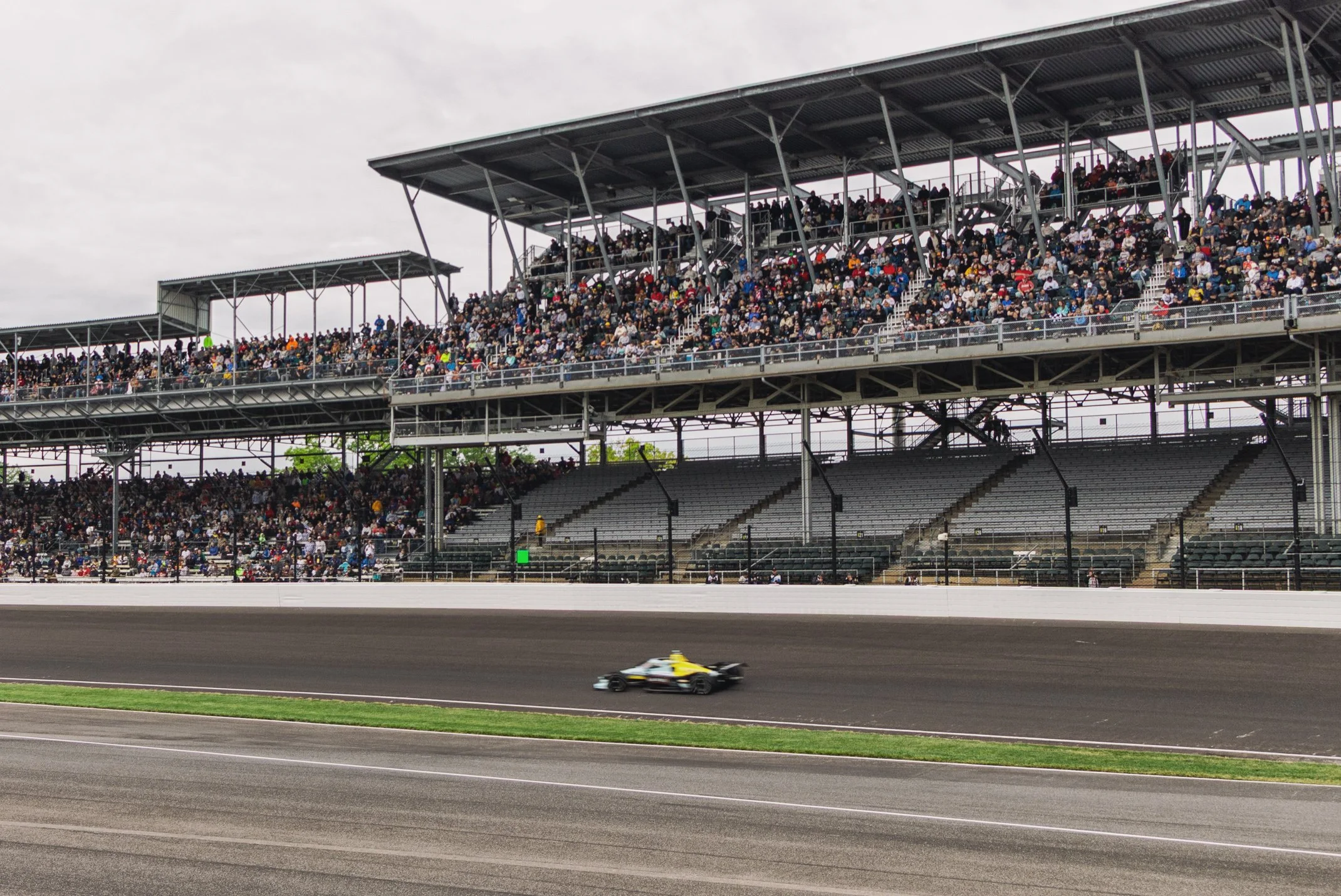Race car speeding on a race track with grandstands full of spectators in the background.