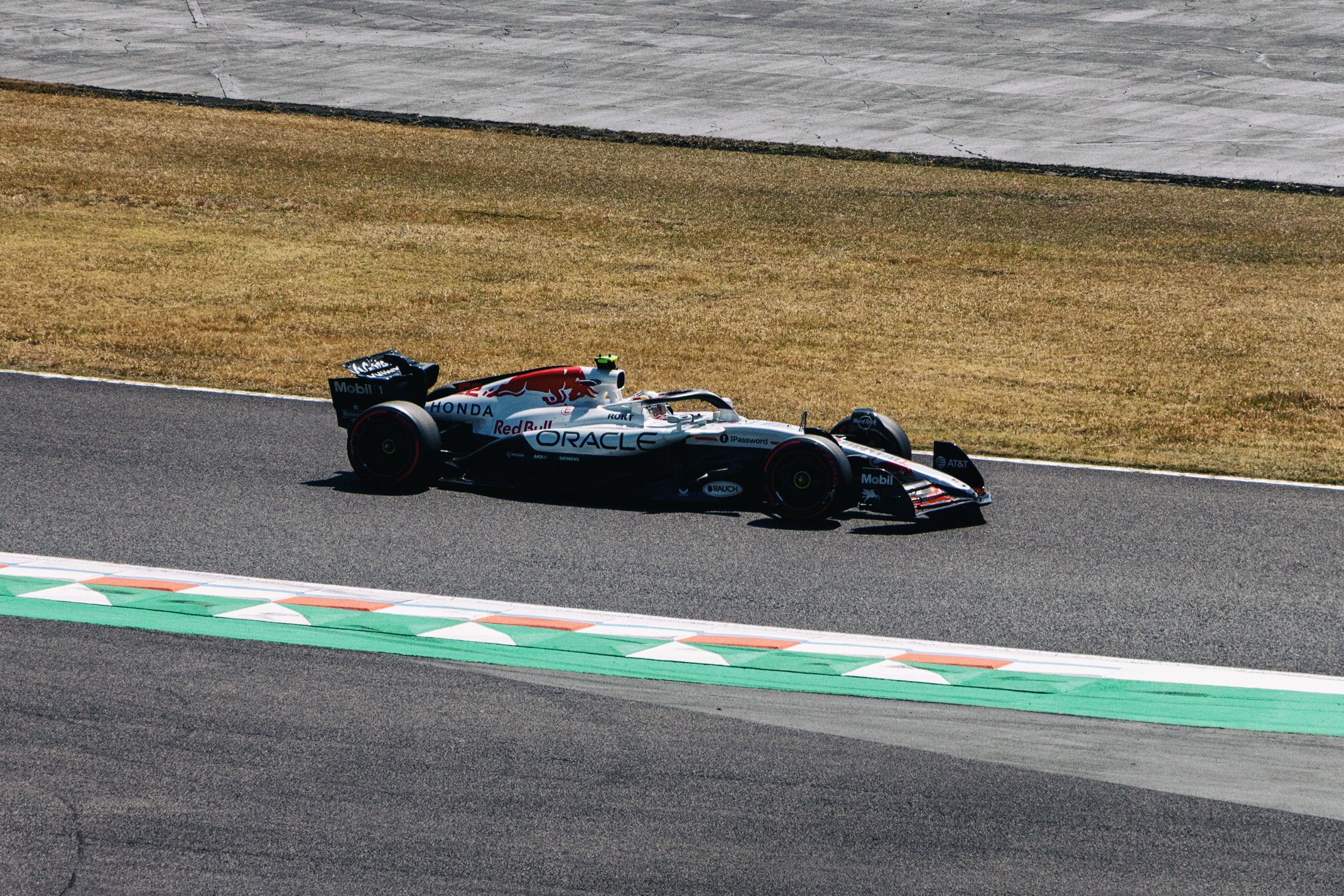 Formula 1 race car on track with sponsor logos, driven on asphalt section near grassy area.